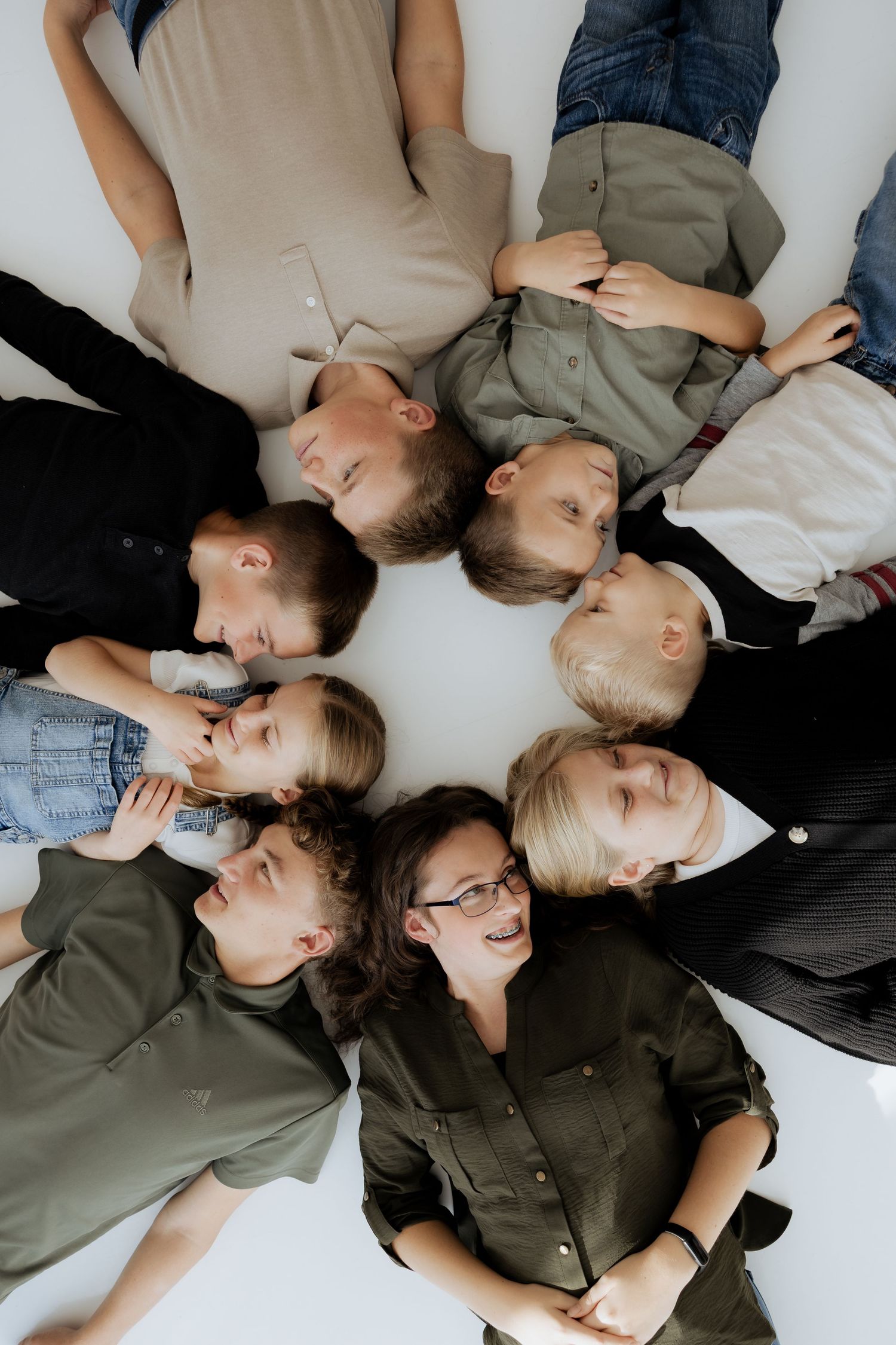 Aerial view of mother with glasses and seven children lying in a circle smiling.