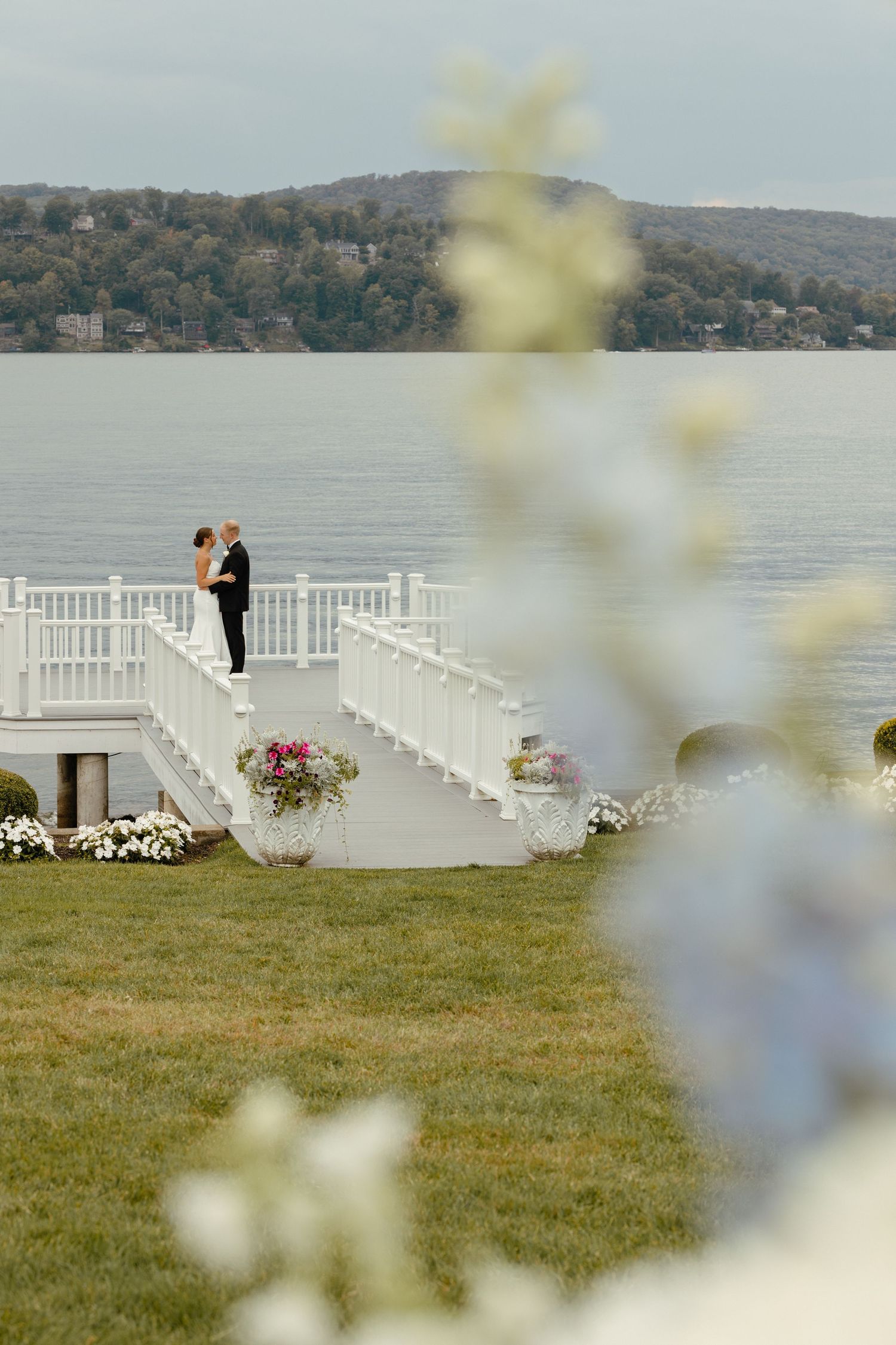 Bride and groom kissing on a white staircase overlooking a serene lake with mountain views.