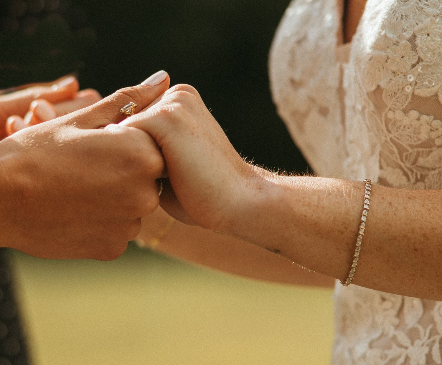 Close-up of bride placing wedding ring on partner's hand during outdoor ceremony.