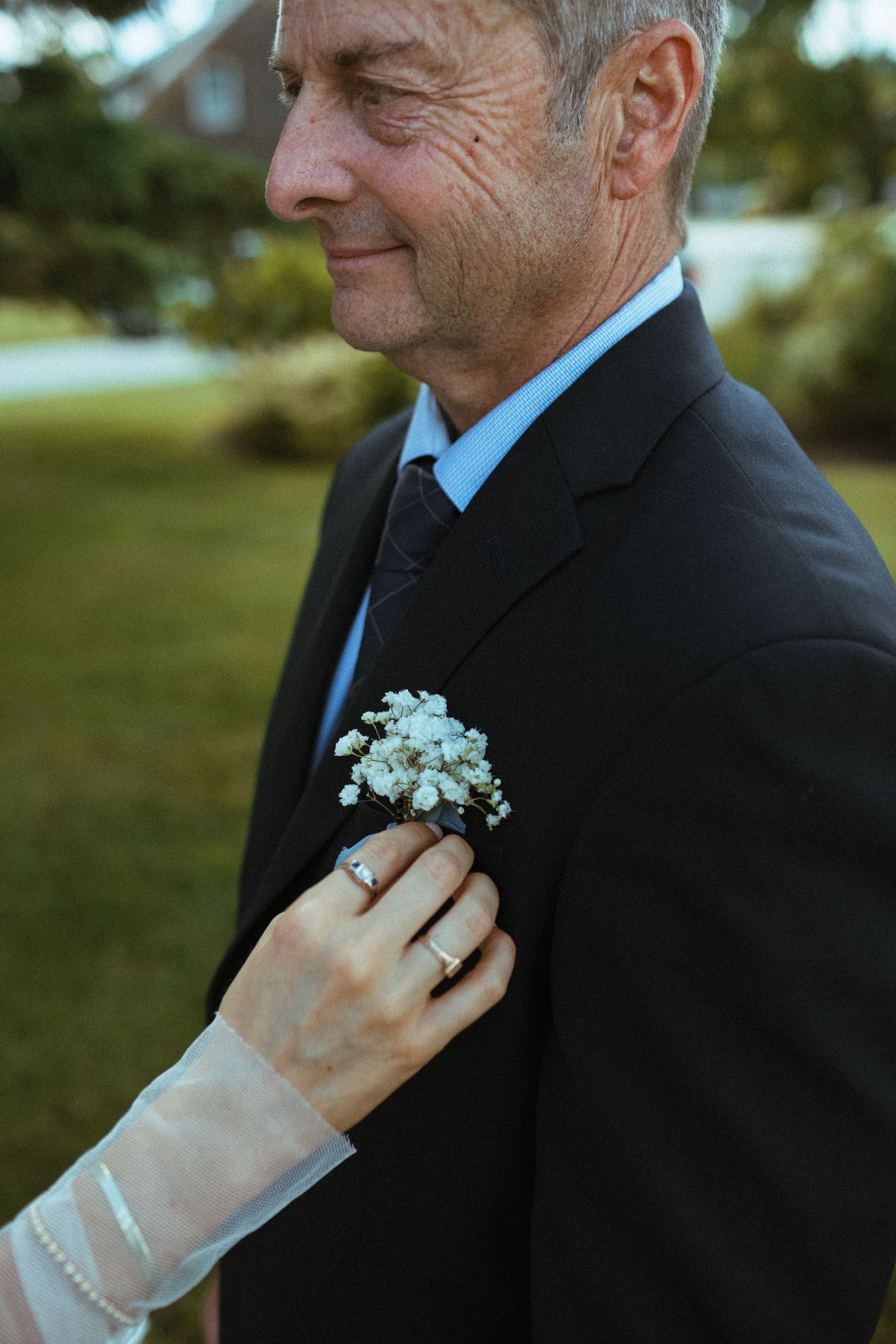 Bride pinning white baby's breath boutonniere on father's dark suit lapel.
