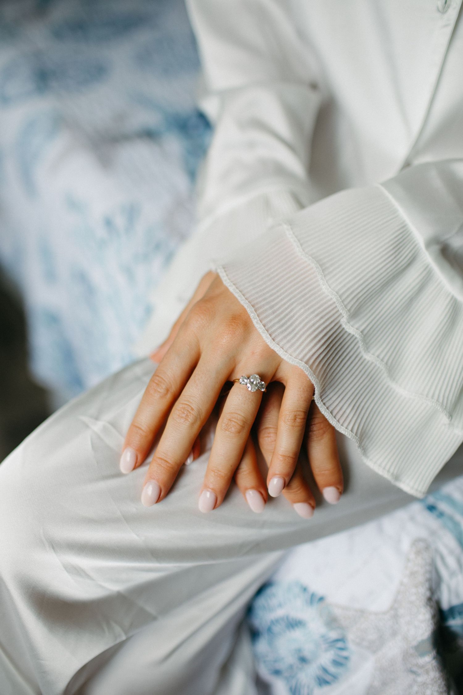 Close-up of bride's hands showing stunning diamond engagement ring with French manicure on wedding day.
