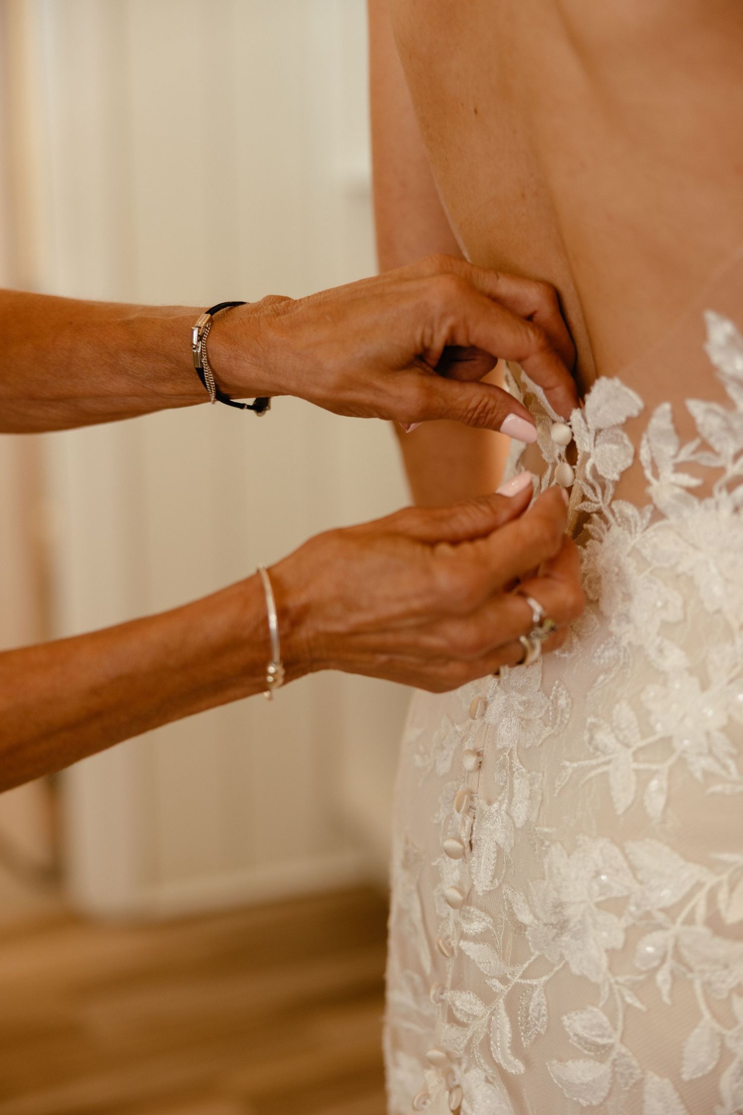Hands carefully fastening lace buttons on back of intricate floral applique wedding gown.