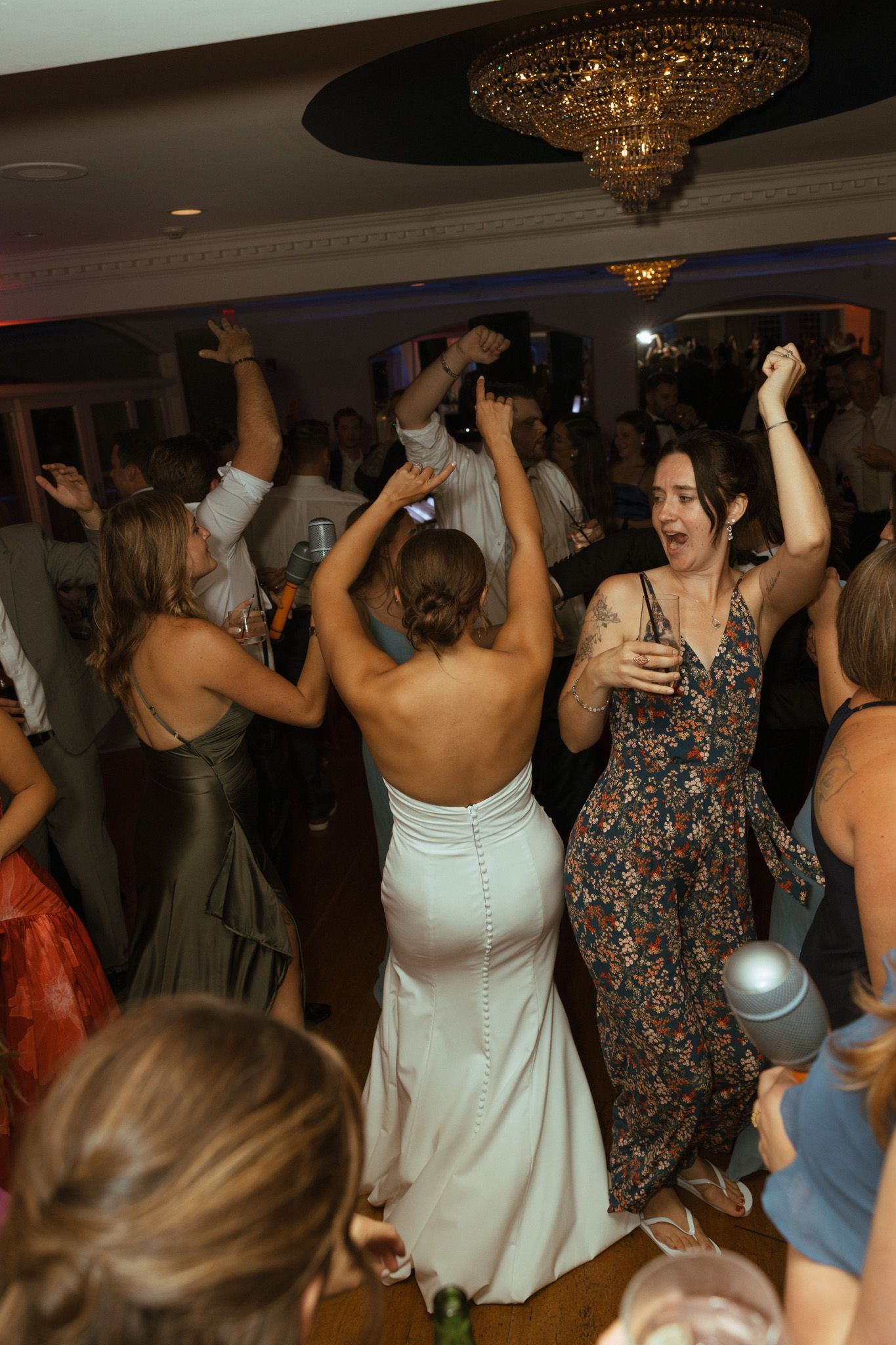 Bride in white backless gown dancing energetically with guests at lively wedding reception party.