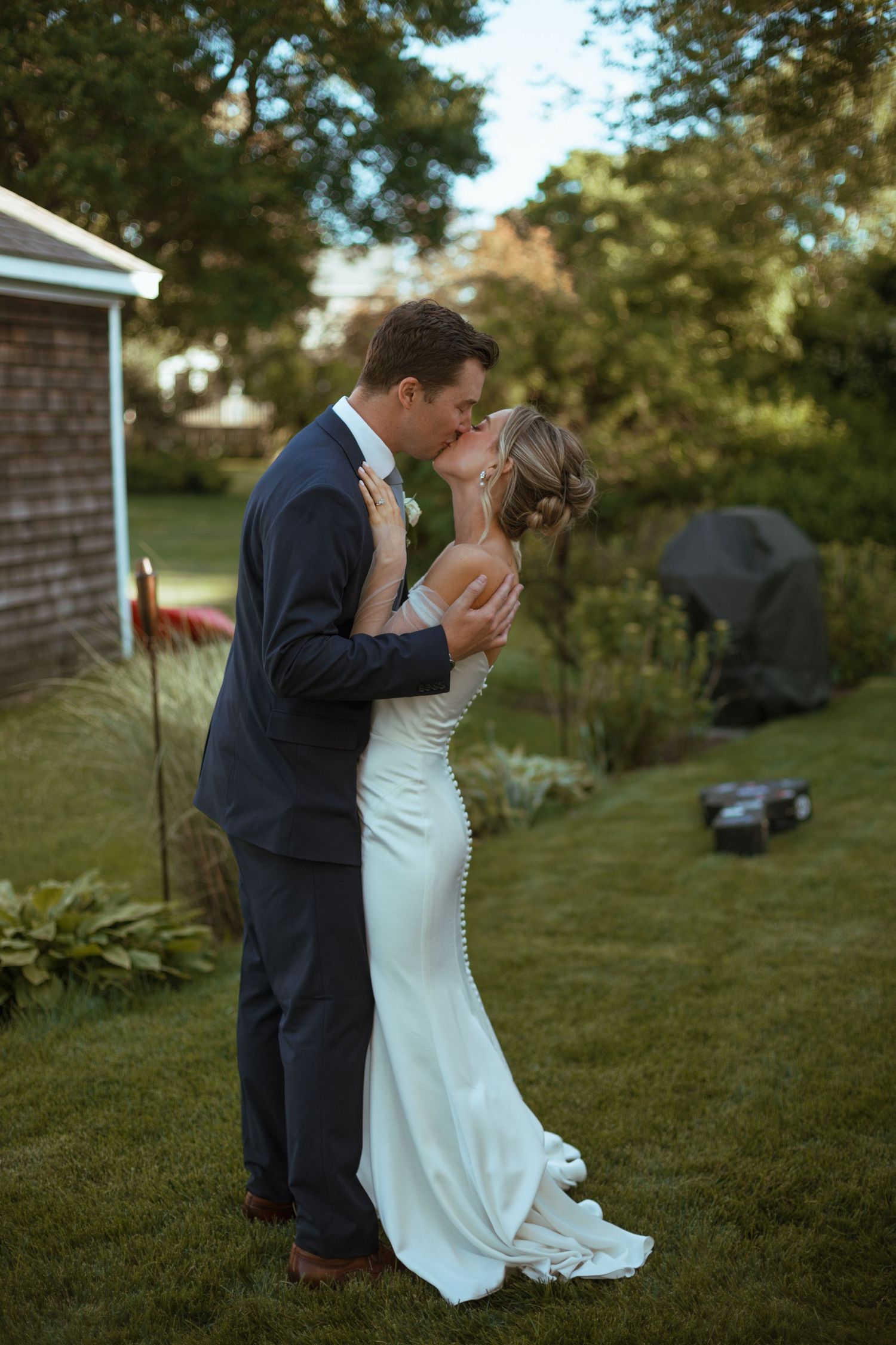 Bride and groom sharing romantic kiss on garden lawn at golden hour outdoor wedding.