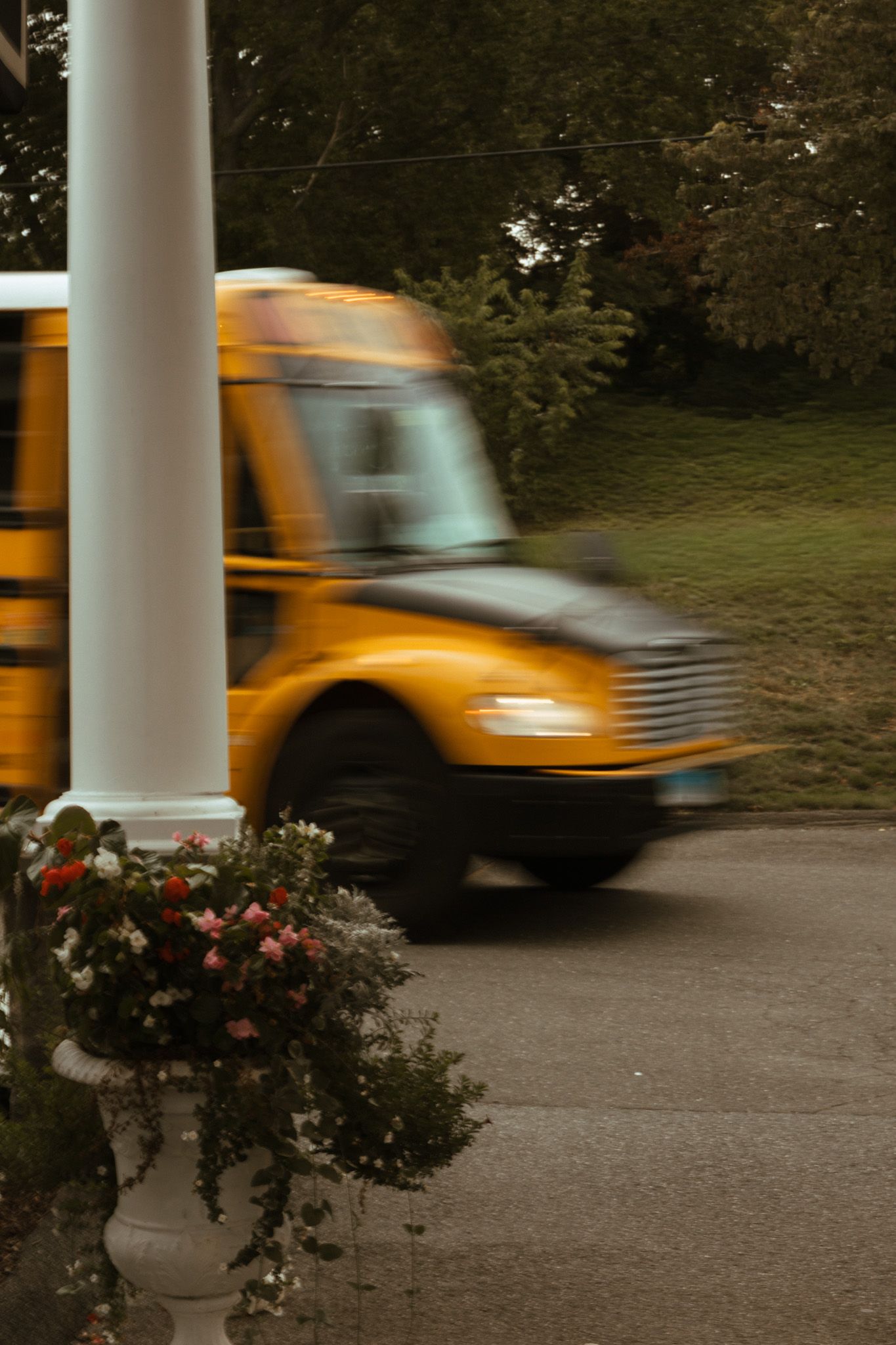 A yellow school bus passing a white column and floral arrangement at a wedding venue entrance.