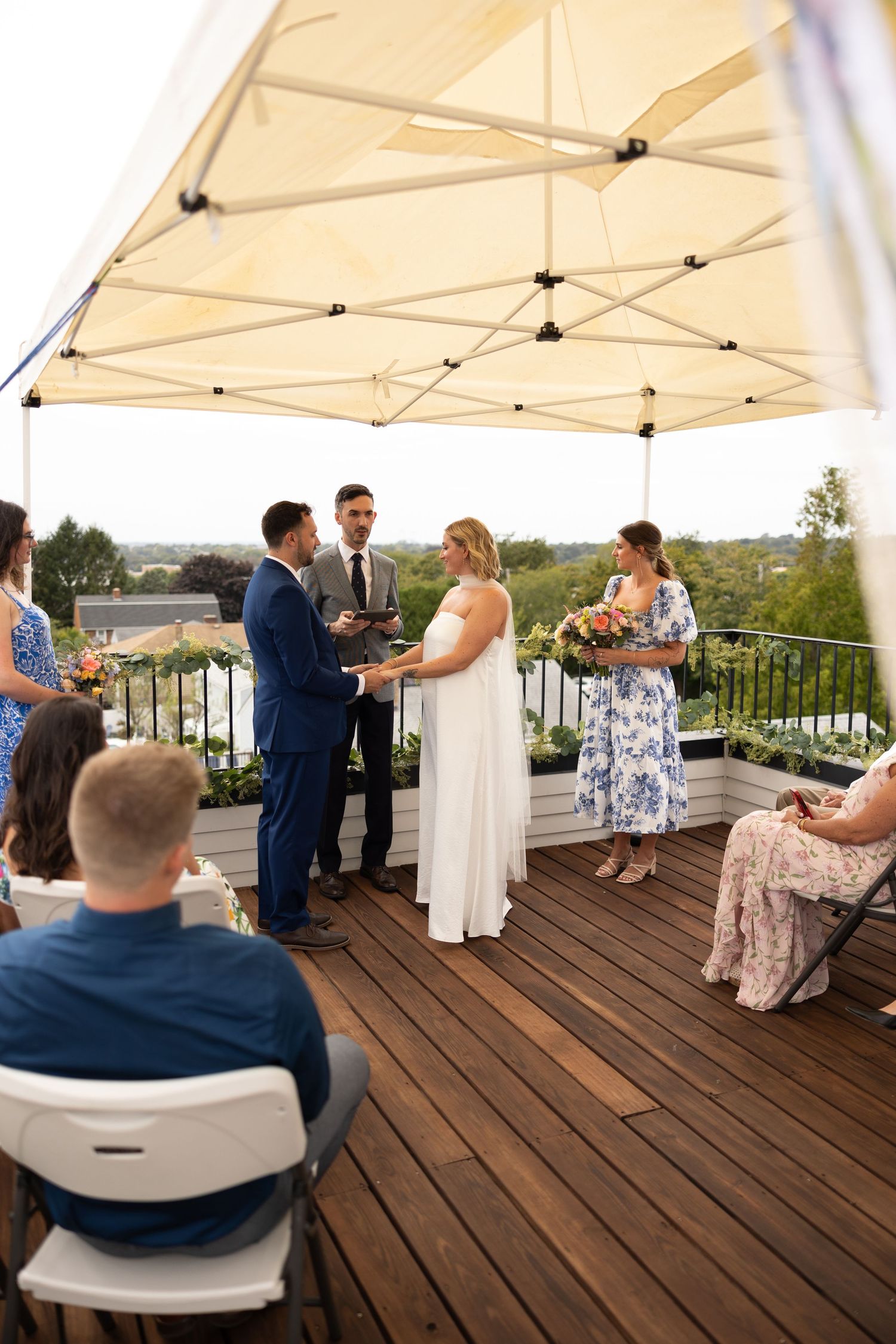 Small intimate wedding ceremony on a wooden rooftop deck under a white canopy with seated guests.