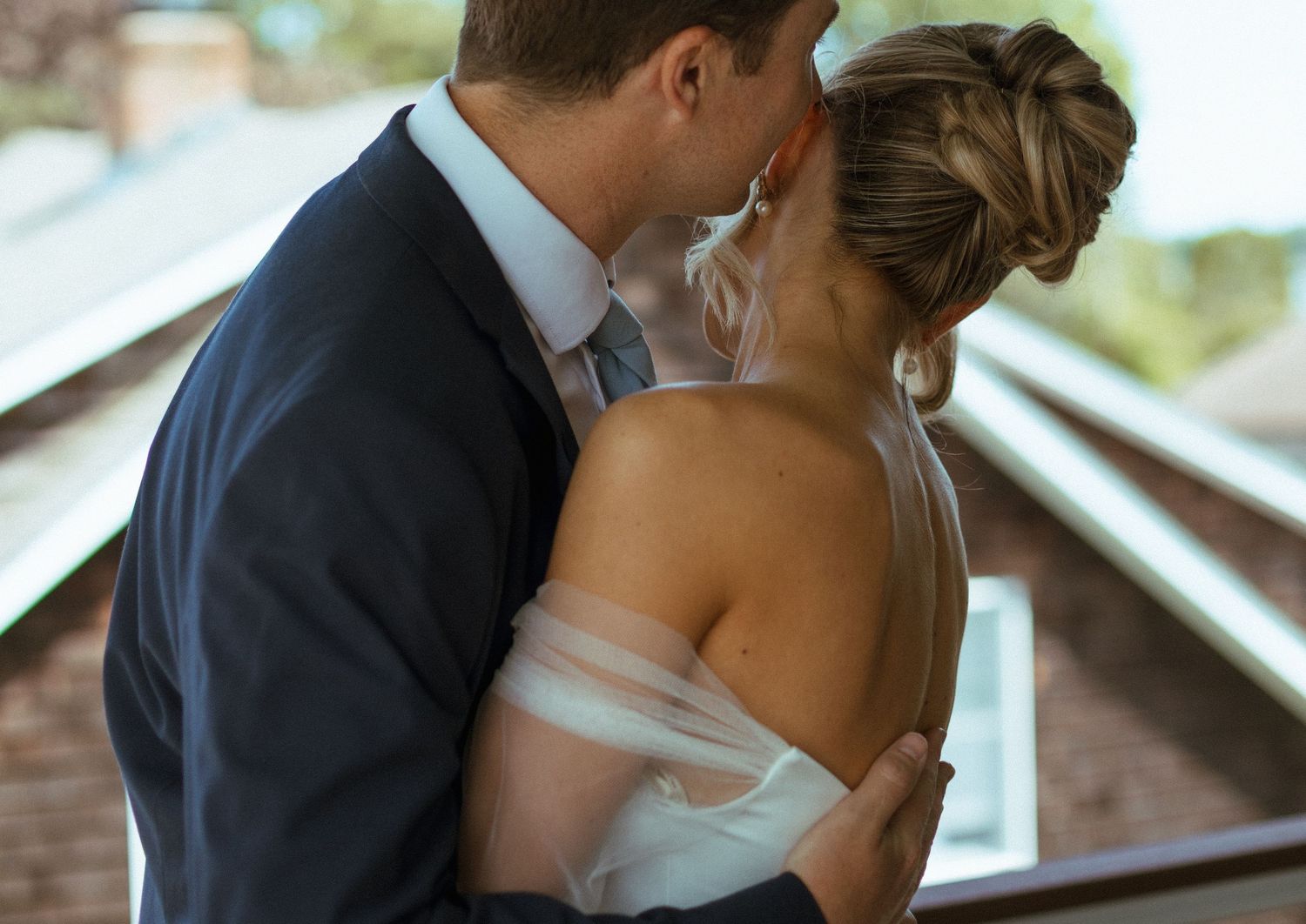 Newlywed couple sharing romantic kiss with groom in navy suit and bride in off-shoulder gown.
