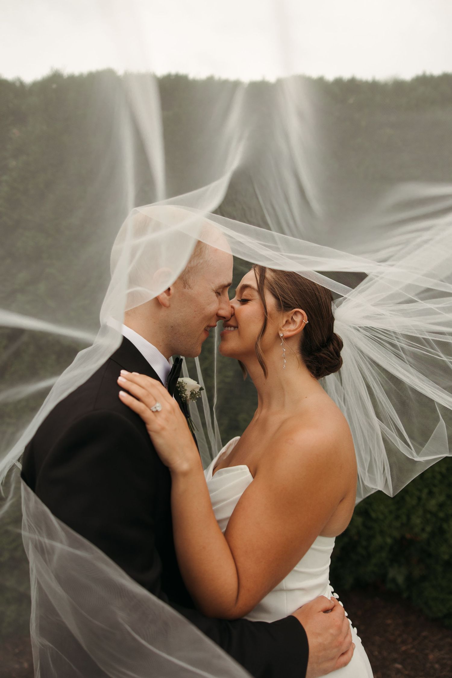 Bride and groom nearly kissing under billowing white veil caught in the wind on their wedding day.