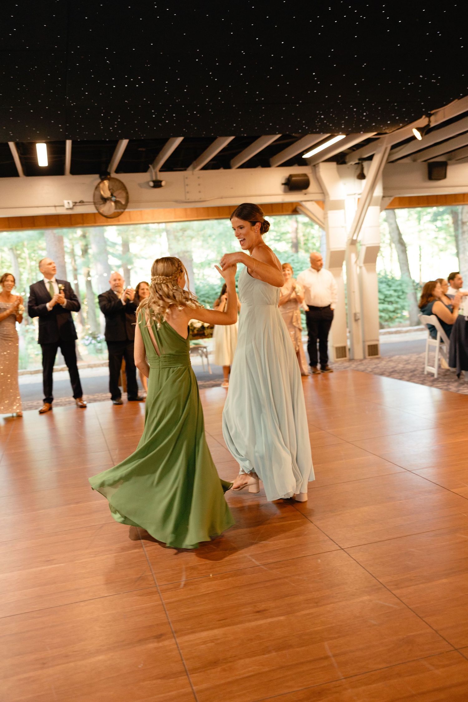 Two women in green and blue gowns sharing emotional dance on wooden floor at wedding reception.film-inspired