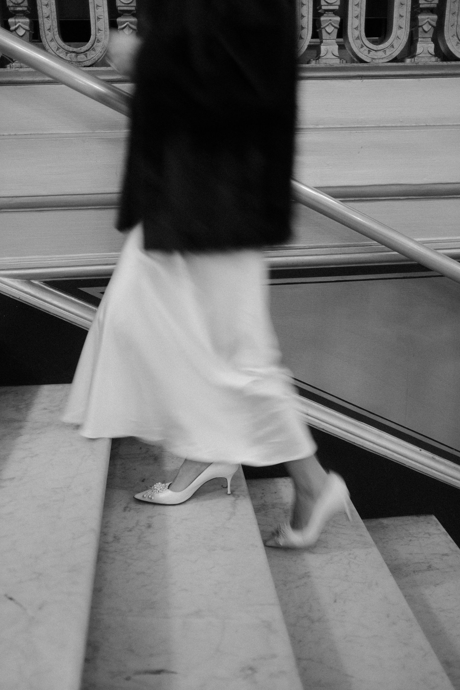 Black and white blurred motion photo of a woman in white dress and fur coat descending marble stairs.film-inspired
