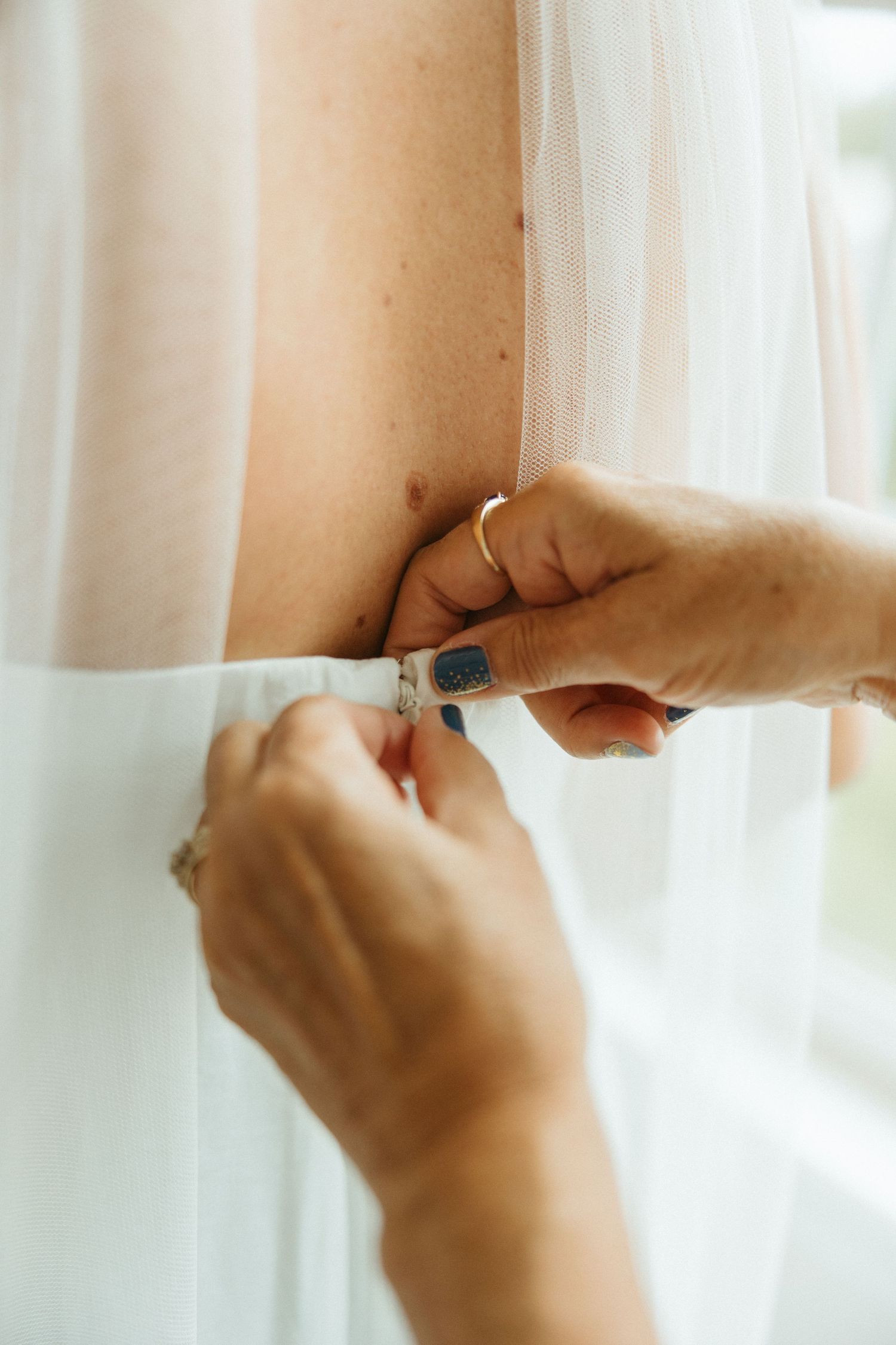 Close-up of hands carefully fastening small buttons on back of white wedding gown.