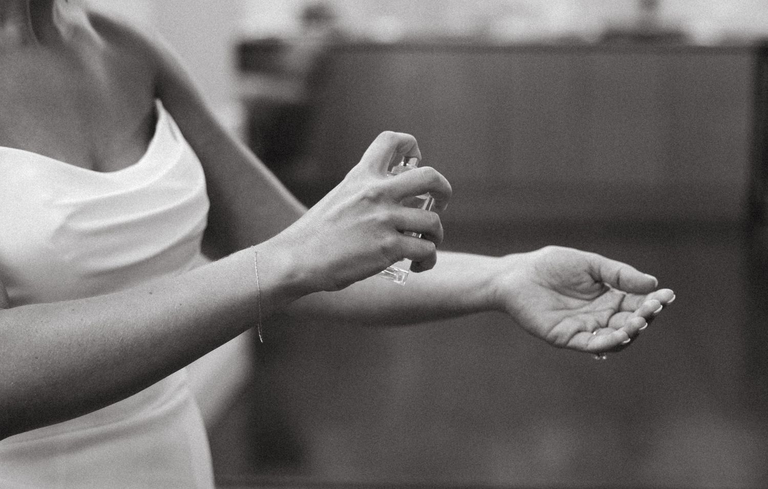 Black and white photo of bride in white dress applying perfume to her wrist.