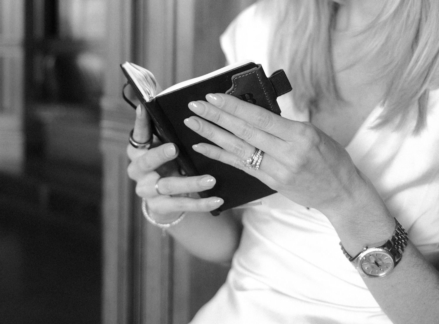 Bride holding small book showing diamond engagement ring and elegant watch, black and white photo.film-inspired