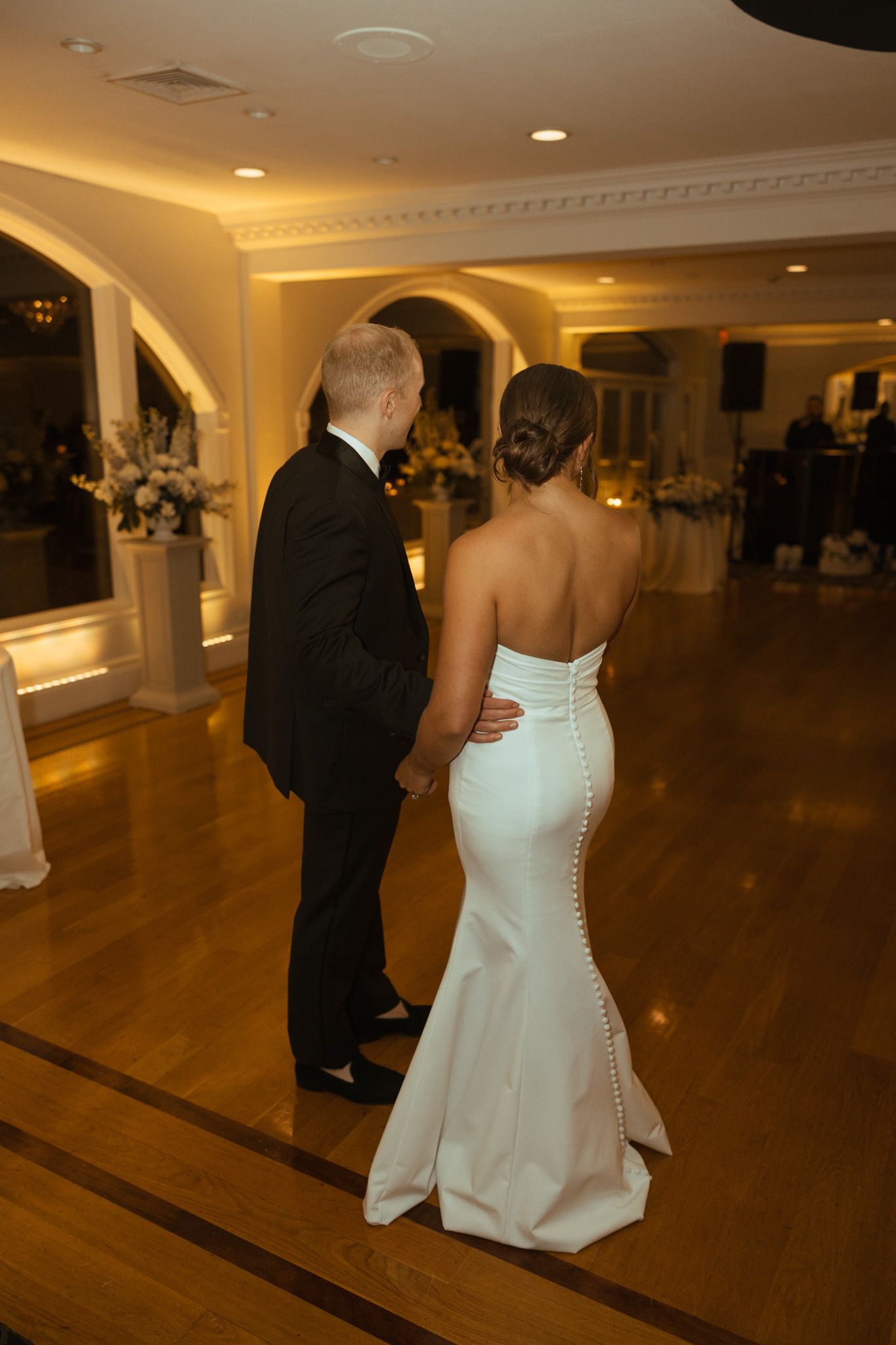 Bride in strapless gown with button back detail holding grooms hand on dance floor.