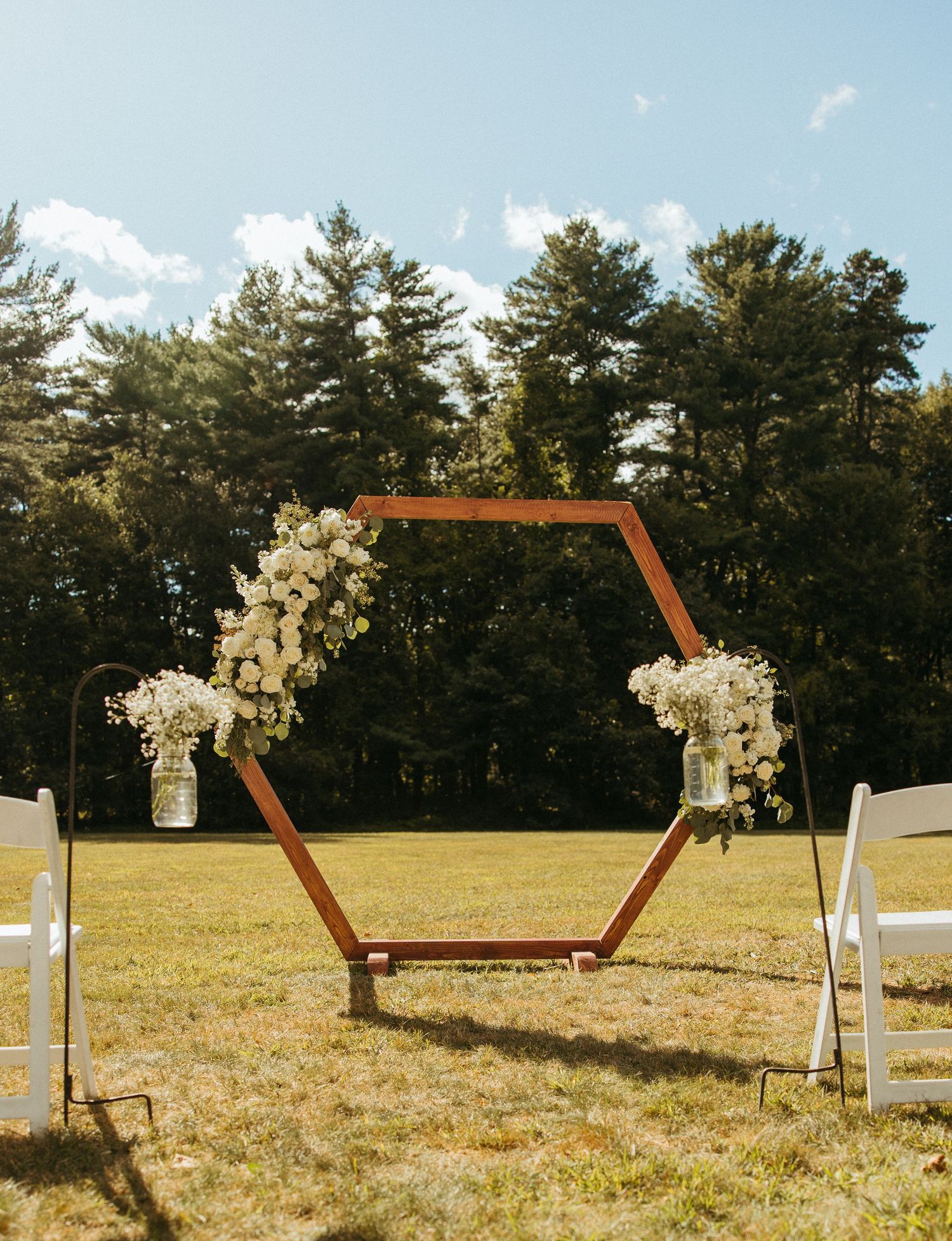 Hexagonal wooden wedding arch adorned with white flowers in outdoor garden setting.