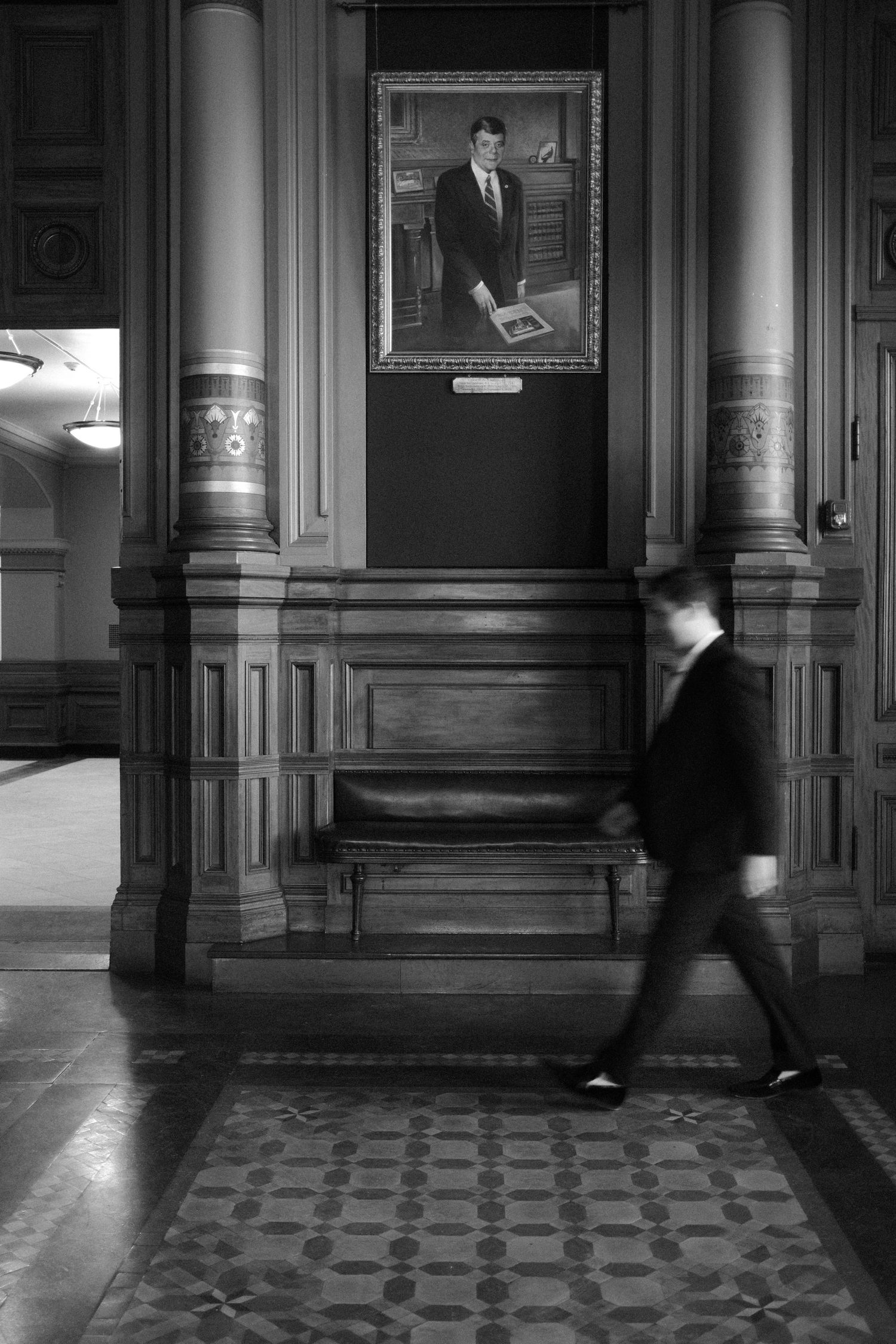 Man in suit walking past portrait in grand historic building hallway.film-inspired