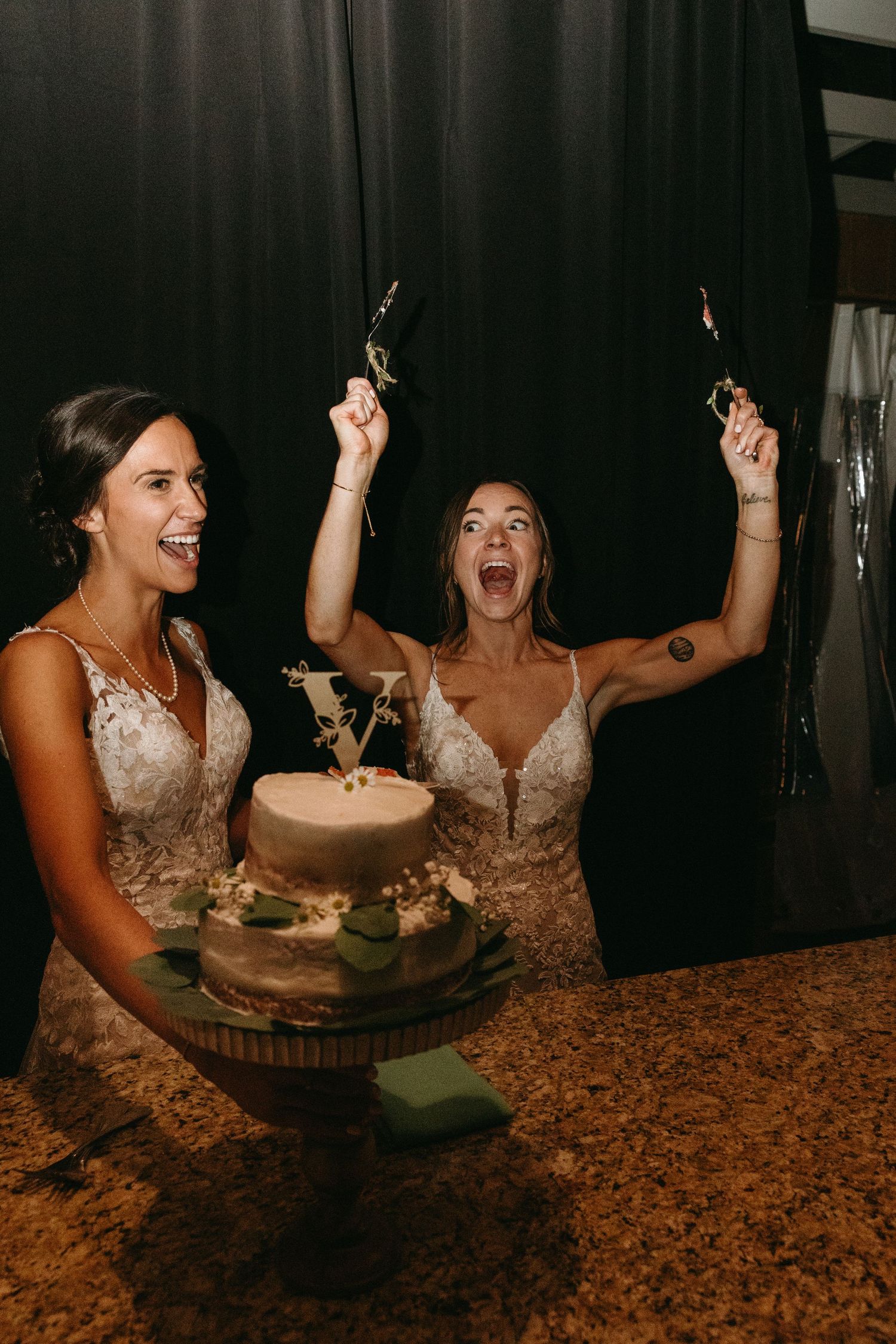 Two brides celebrate with sparklers over wedding cake at reception.film-inspired