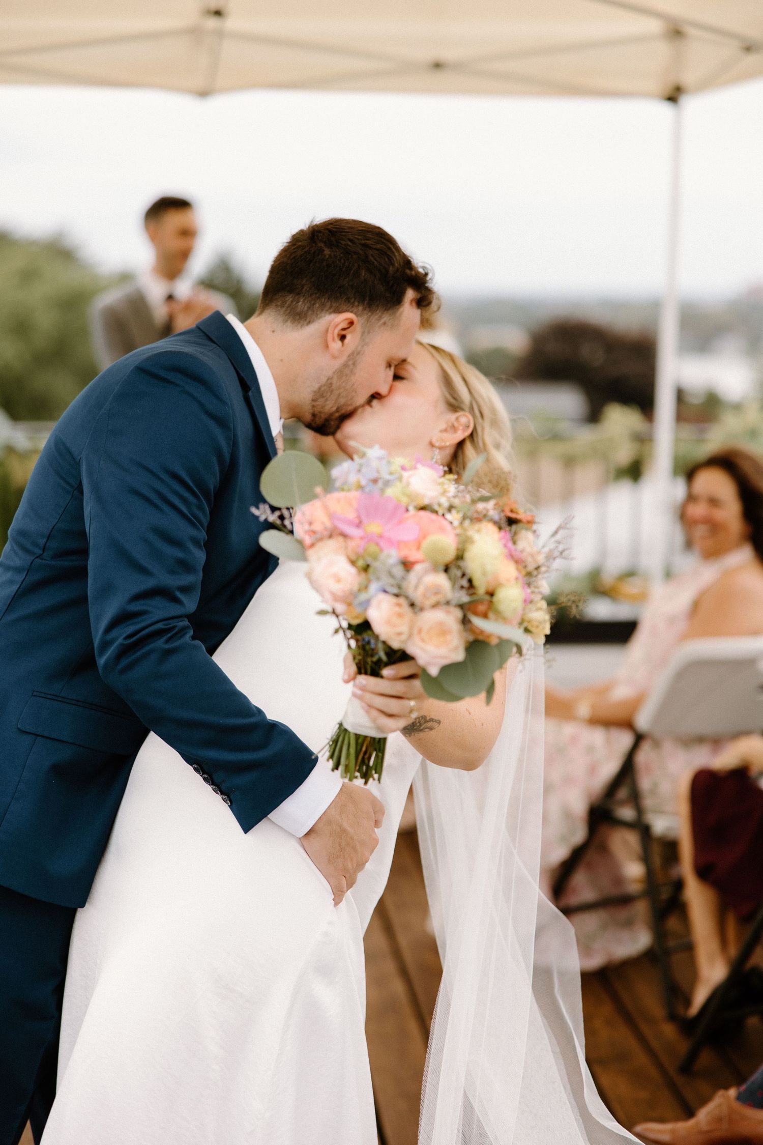 Bride and groom share their first kiss during outdoor rooftop wedding ceremony, bride holds colorful bouquet.