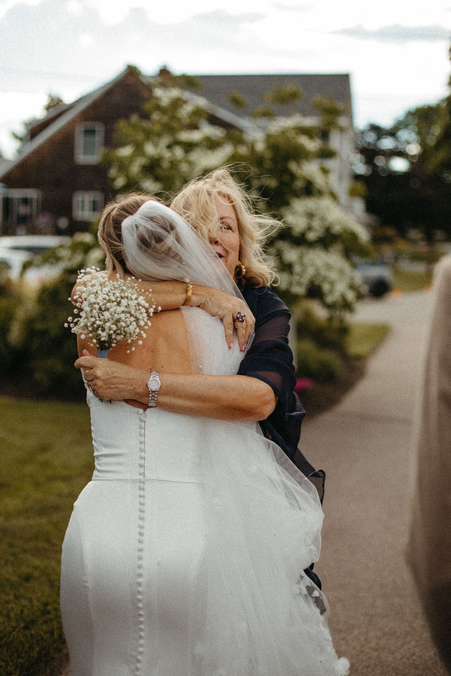 Bride and older woman sharing warm emotional hug outside during wedding day.
