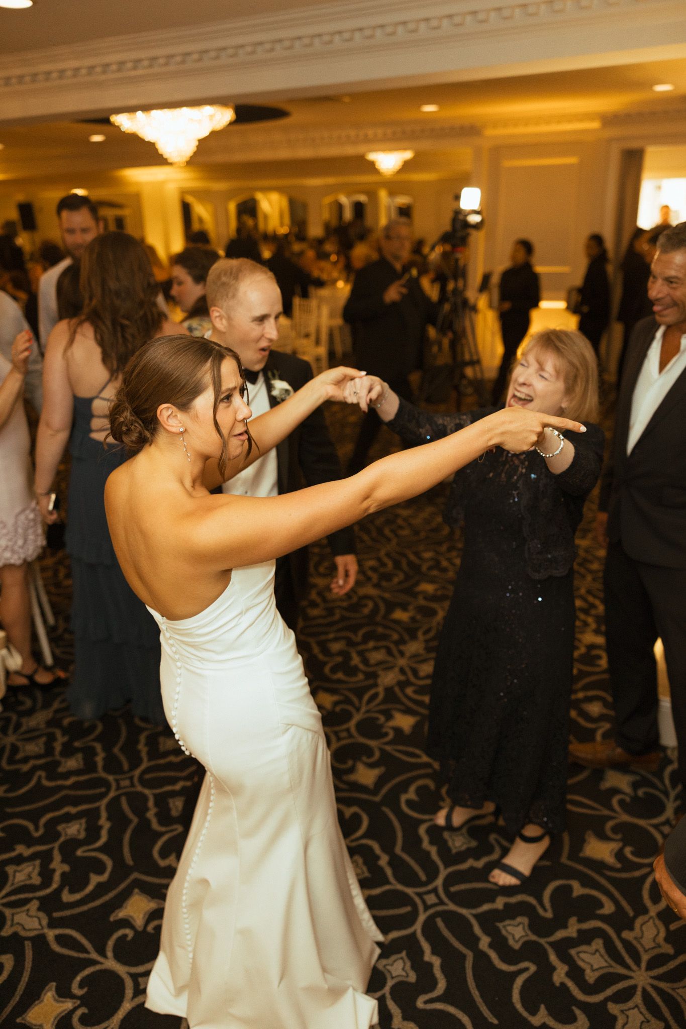 Bride in white gown dancing joyfully with guests at wedding reception.