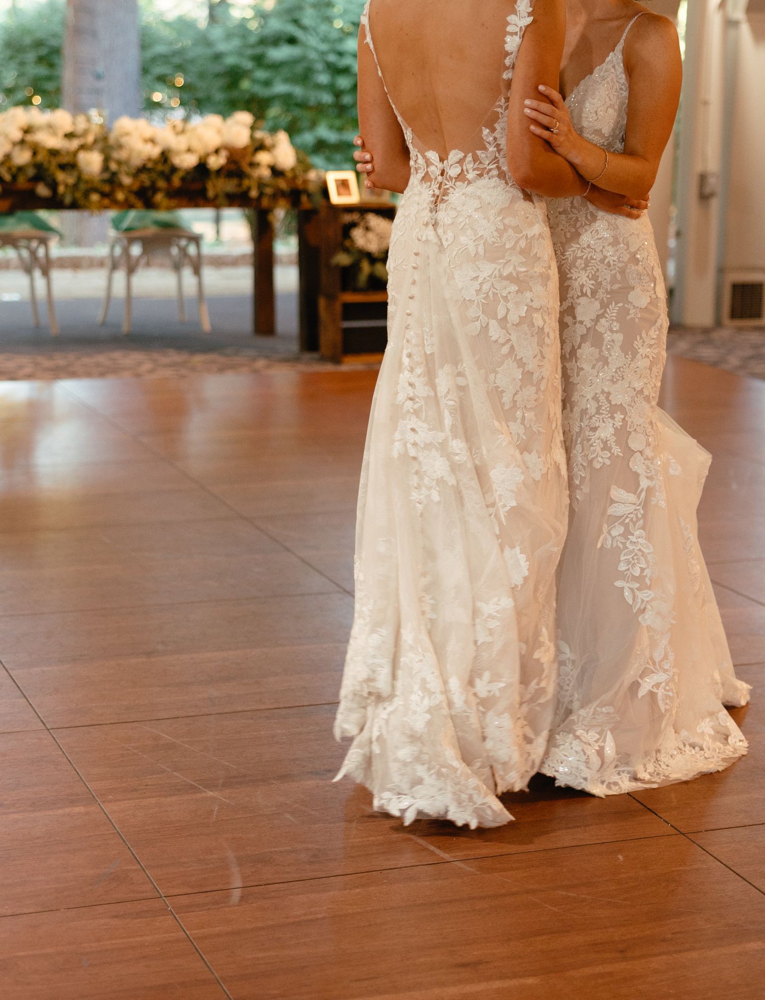 Close-up back view of two brides in lace appliqué wedding gowns dancing together.film-inspired