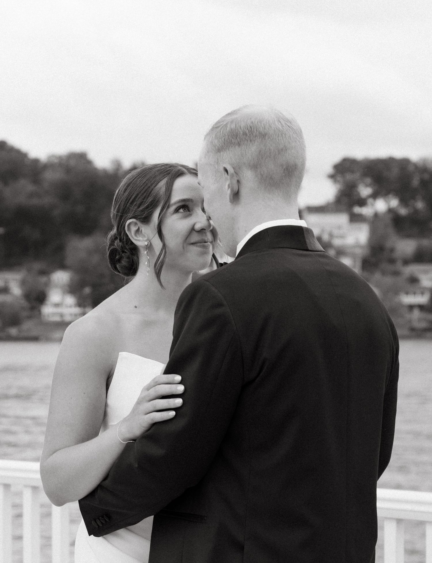 Black and white portrait of a smiling bride and groom sharing a romantic moment by the water.