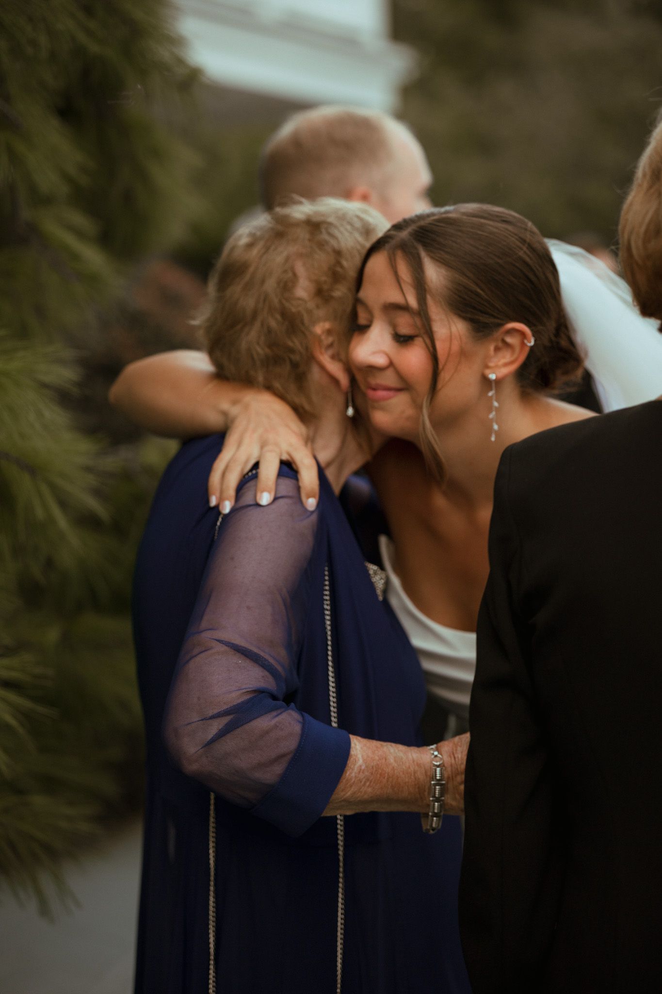 Bride in white gown and veil shares warm hug with guest at wedding reception.