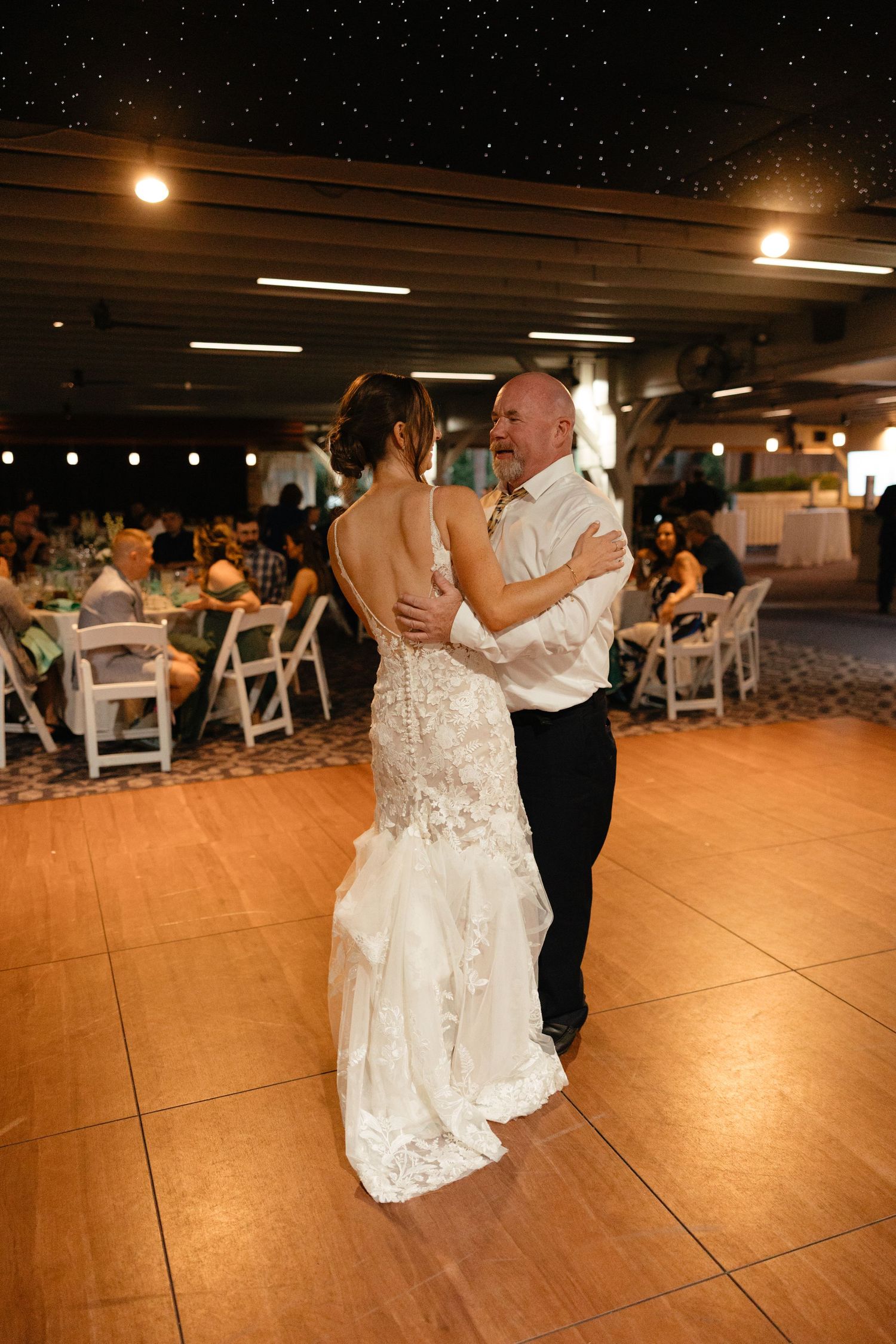 Father-daughter wedding dance at reception with guests seated at decorated tables behind them.film-inspired