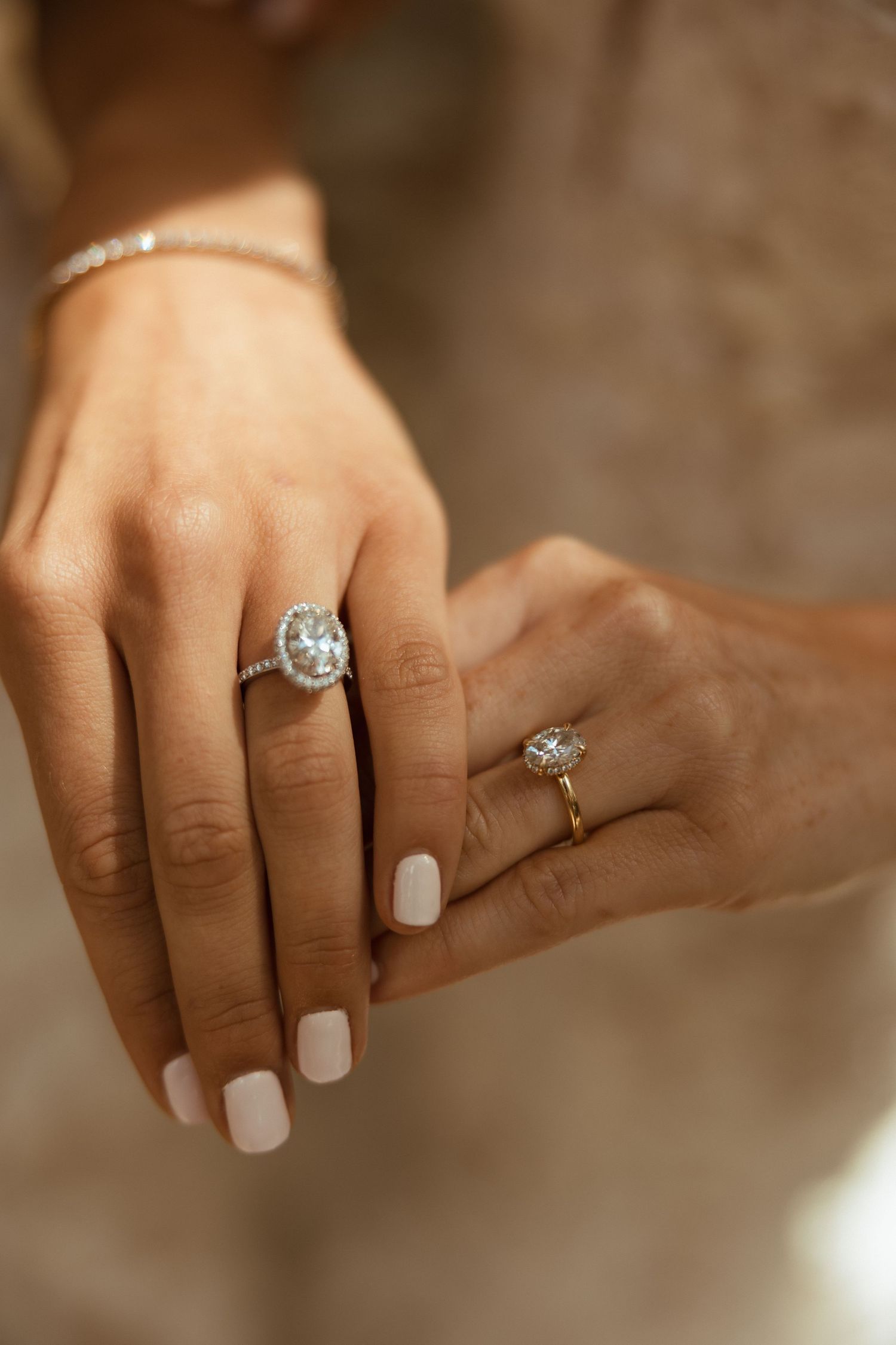 Close-up of two brides showing diamond engagement rings, one silver halo and one gold oval setting.