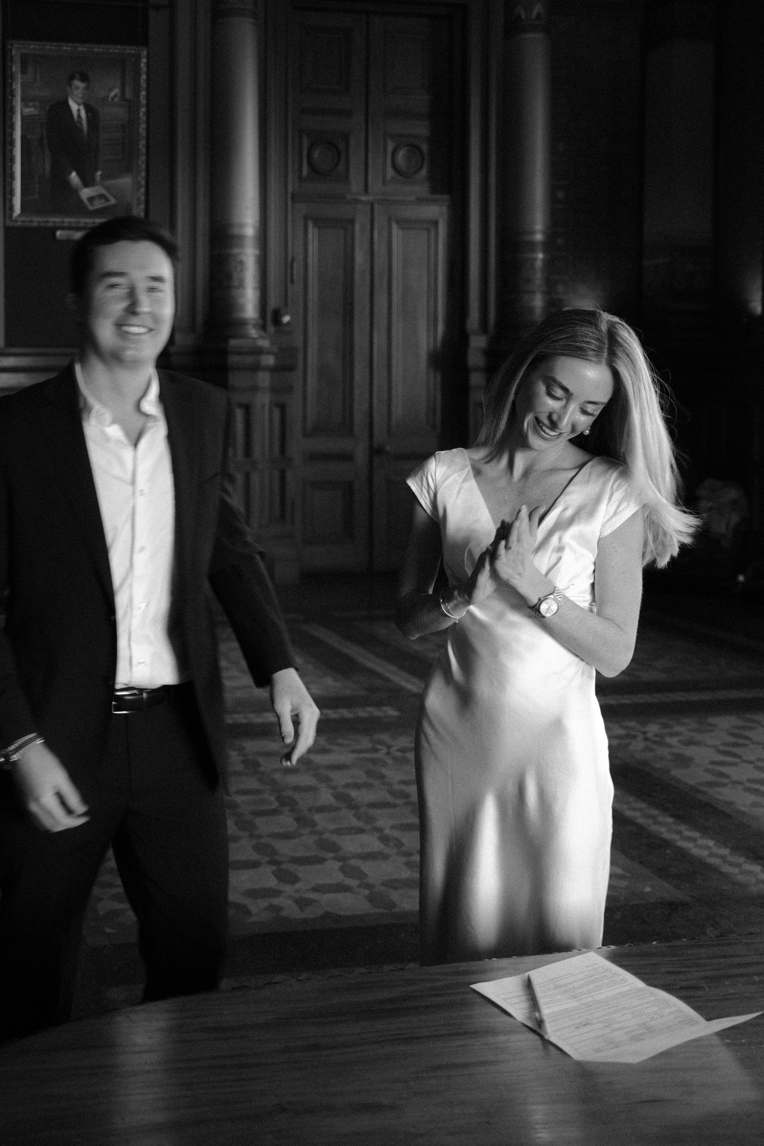 Couple laughing joyfully in an elegant wood-paneled room after signing wedding documents.film-inspired
