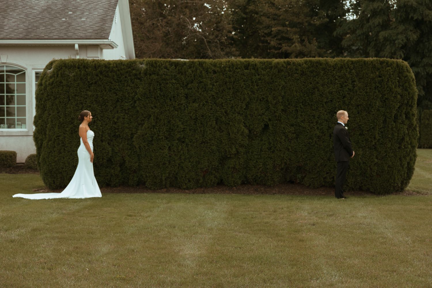 Bride and groom separated by tall hedge for first look moment on wedding day.