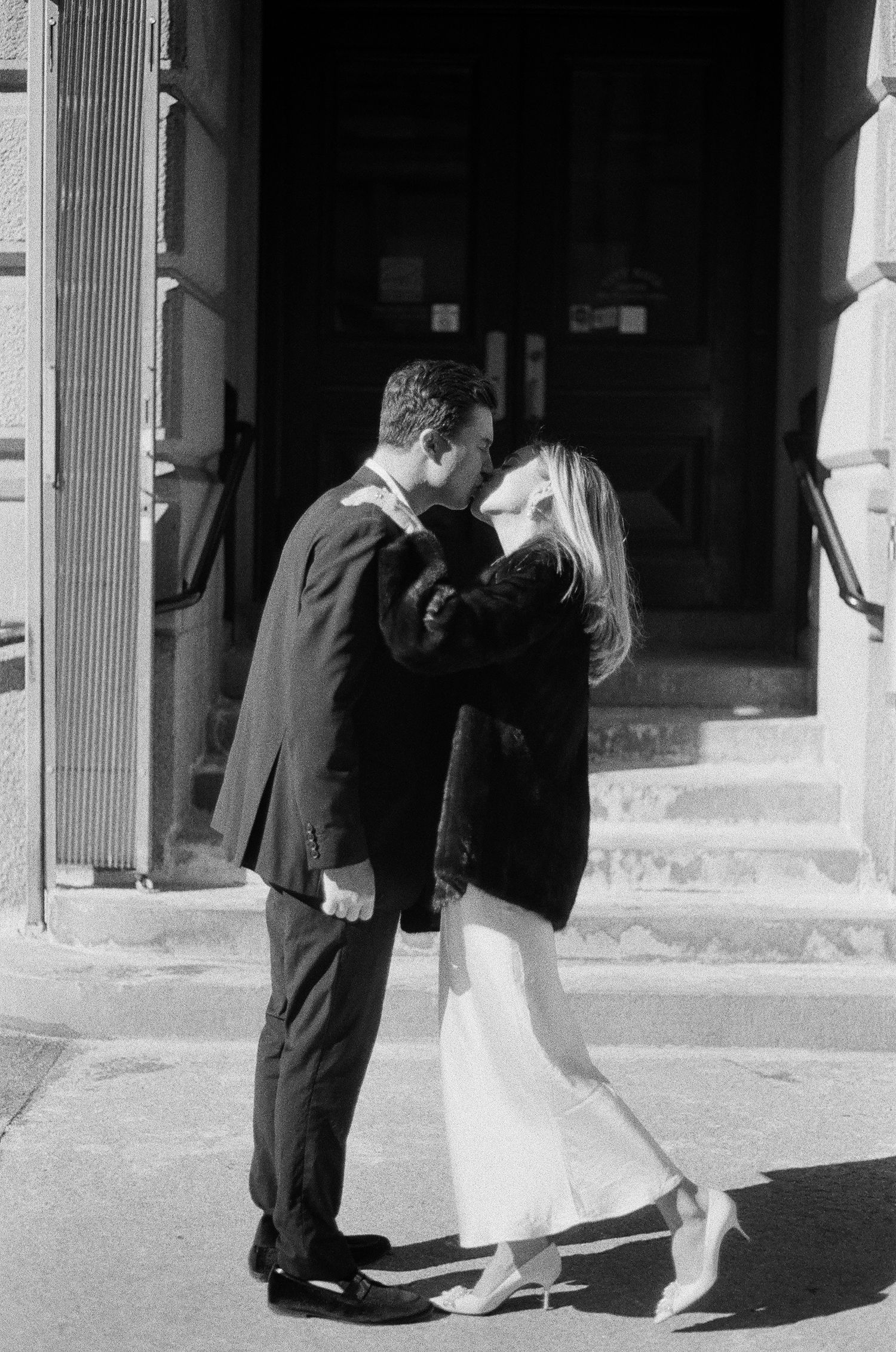 Newlywed couple sharing a kiss outside historic building steps after city hall wedding ceremony. film-inspired