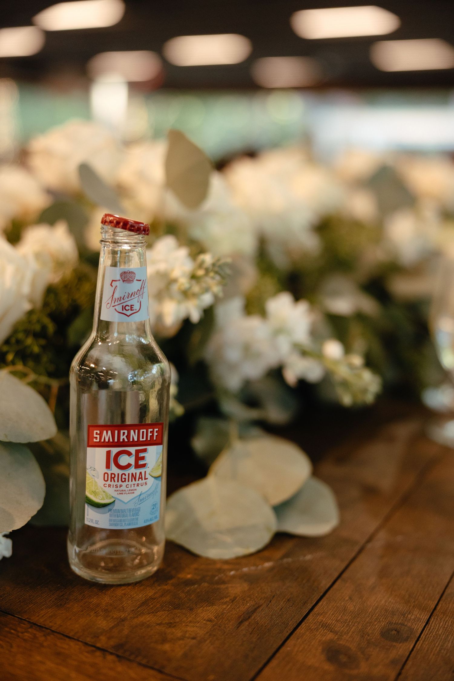 Smirnoff Ice bottle on rustic wood table with white floral centerpiece at wedding reception.film-inspired