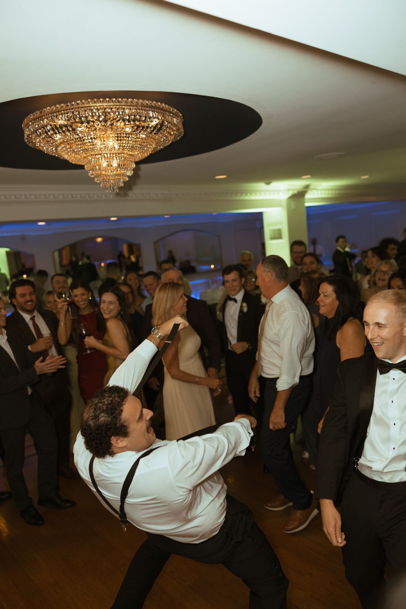 Wedding guest energetically dancing under crystal chandelier at lively reception party.