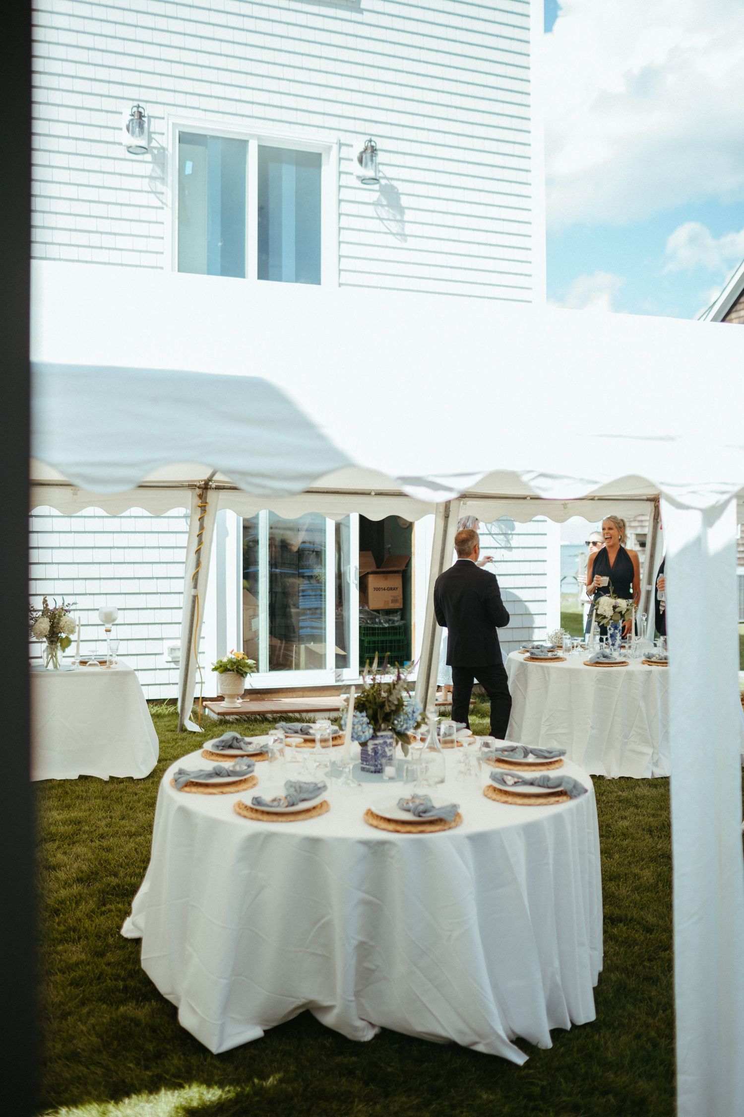 Elegant outdoor wedding reception setup with white tablecloths and tent beside a white coastal venue.