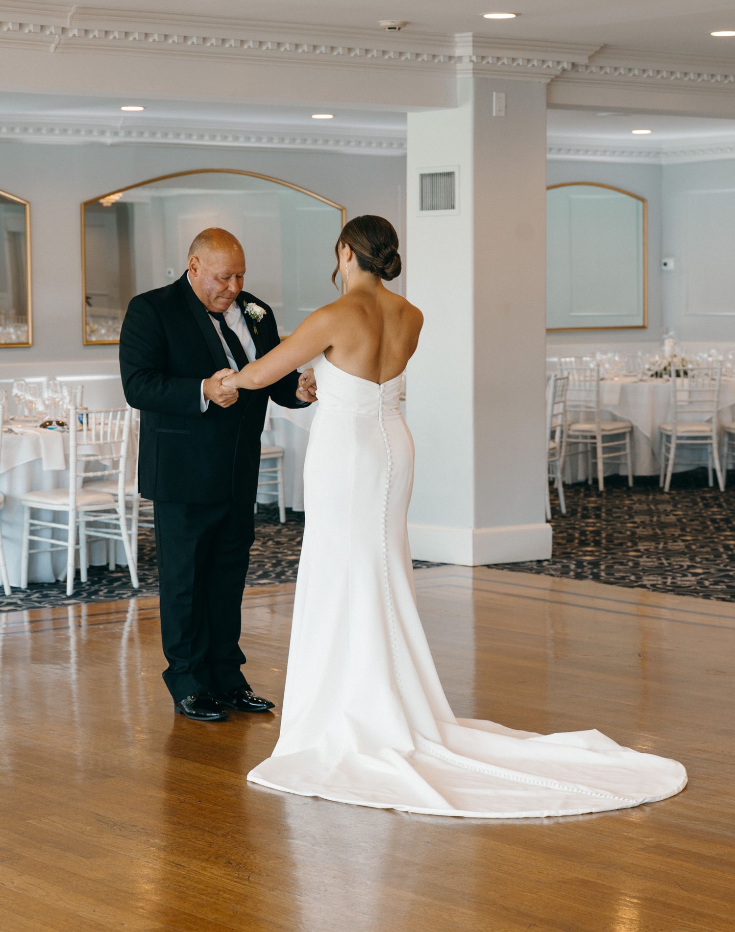 Bride and father sharing first dance on wooden dance floor at elegant wedding reception.
