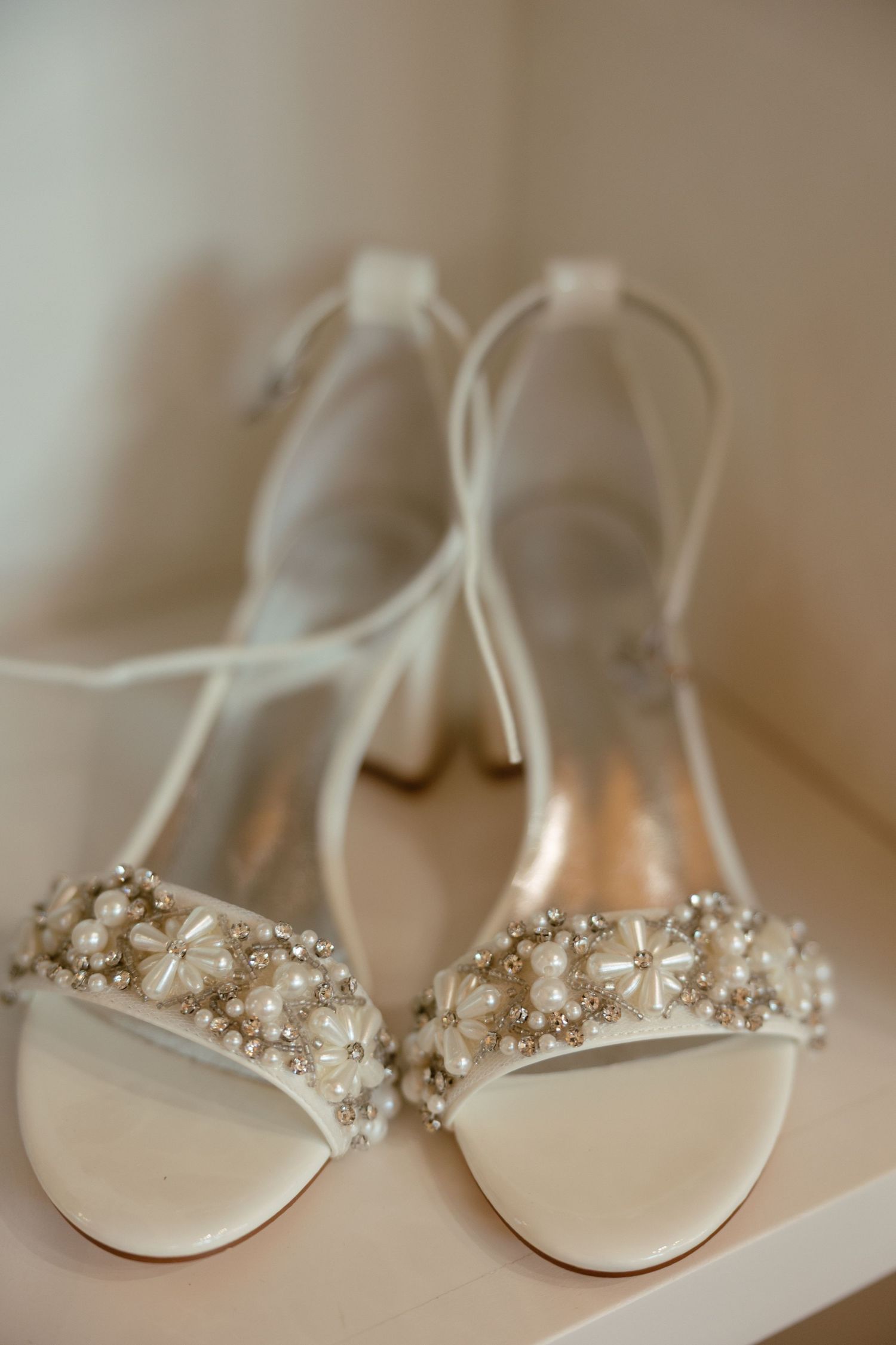 White bridal block heel sandals adorned with pearl and crystal floral embellishments on shelf.