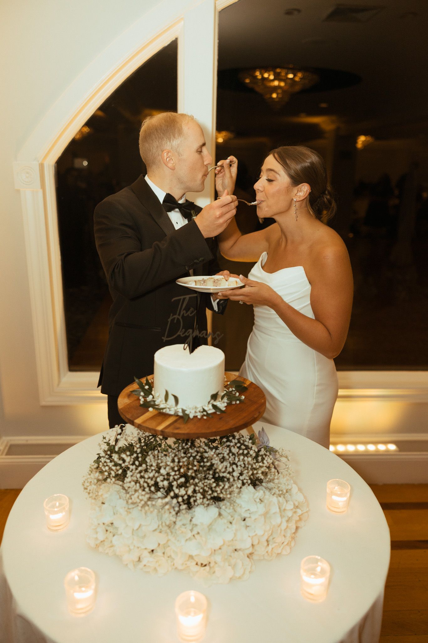 Bride and groom feeding each other wedding cake surrounded by candles and flowers.