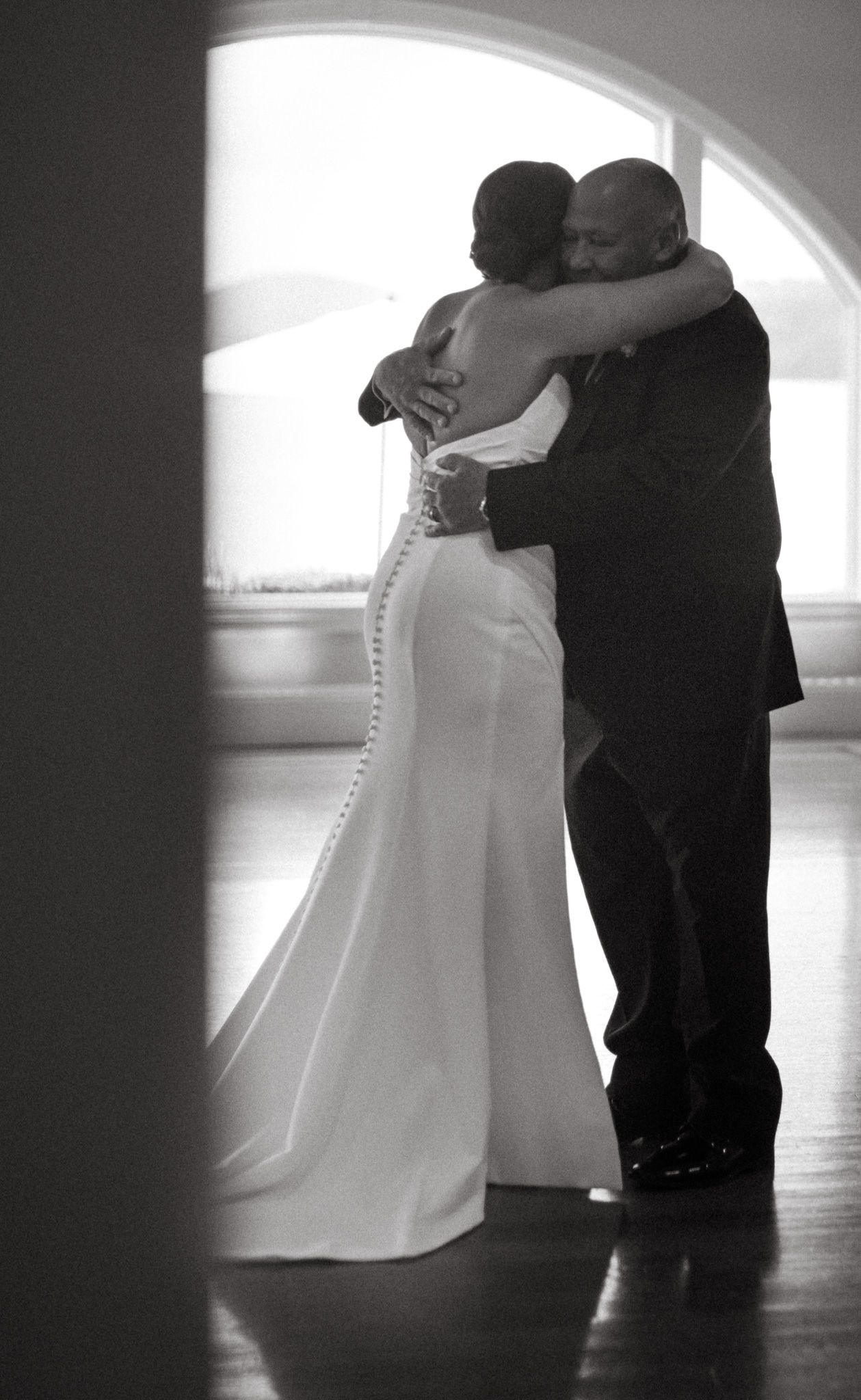 Black and white photo of a bride and groom sharing a tender embrace during their first dance at wedding reception.