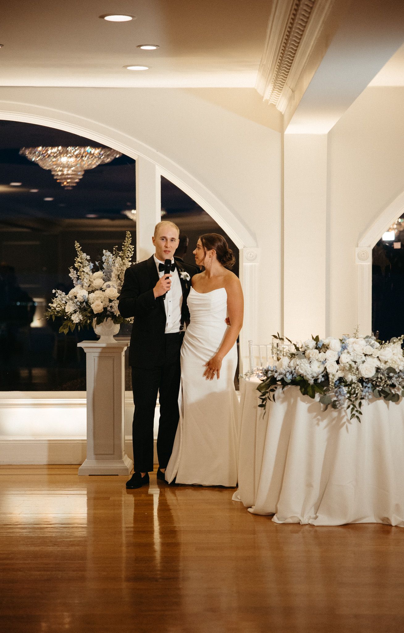 Bride and groom standing together at elegant wedding reception with floral arrangements.