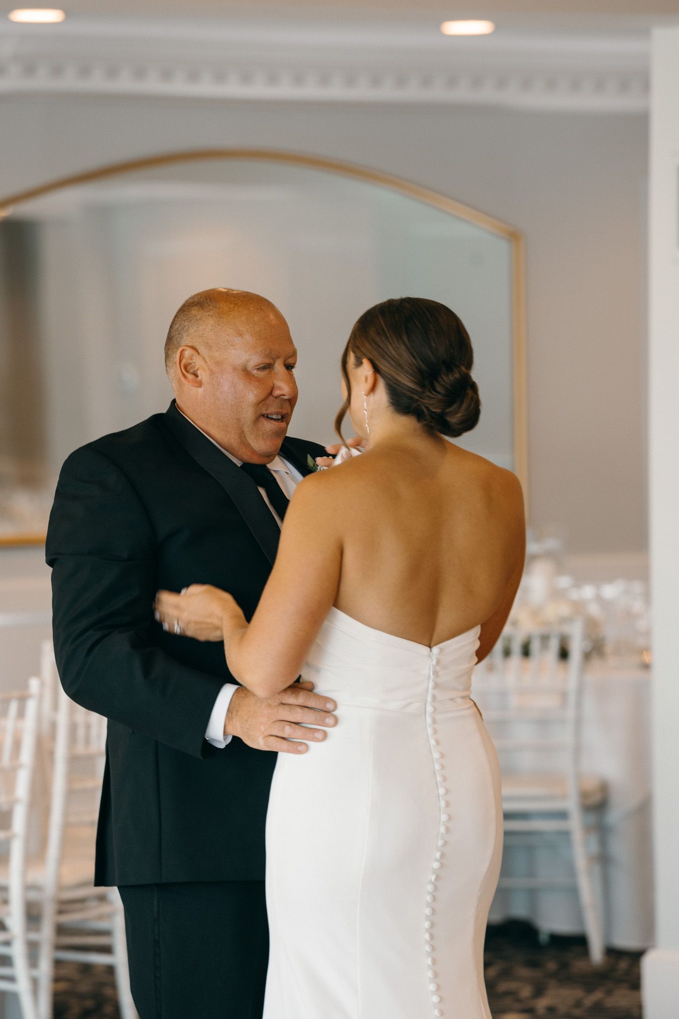 Emotional father-daughter first dance at wedding reception in elegant white ballroom.