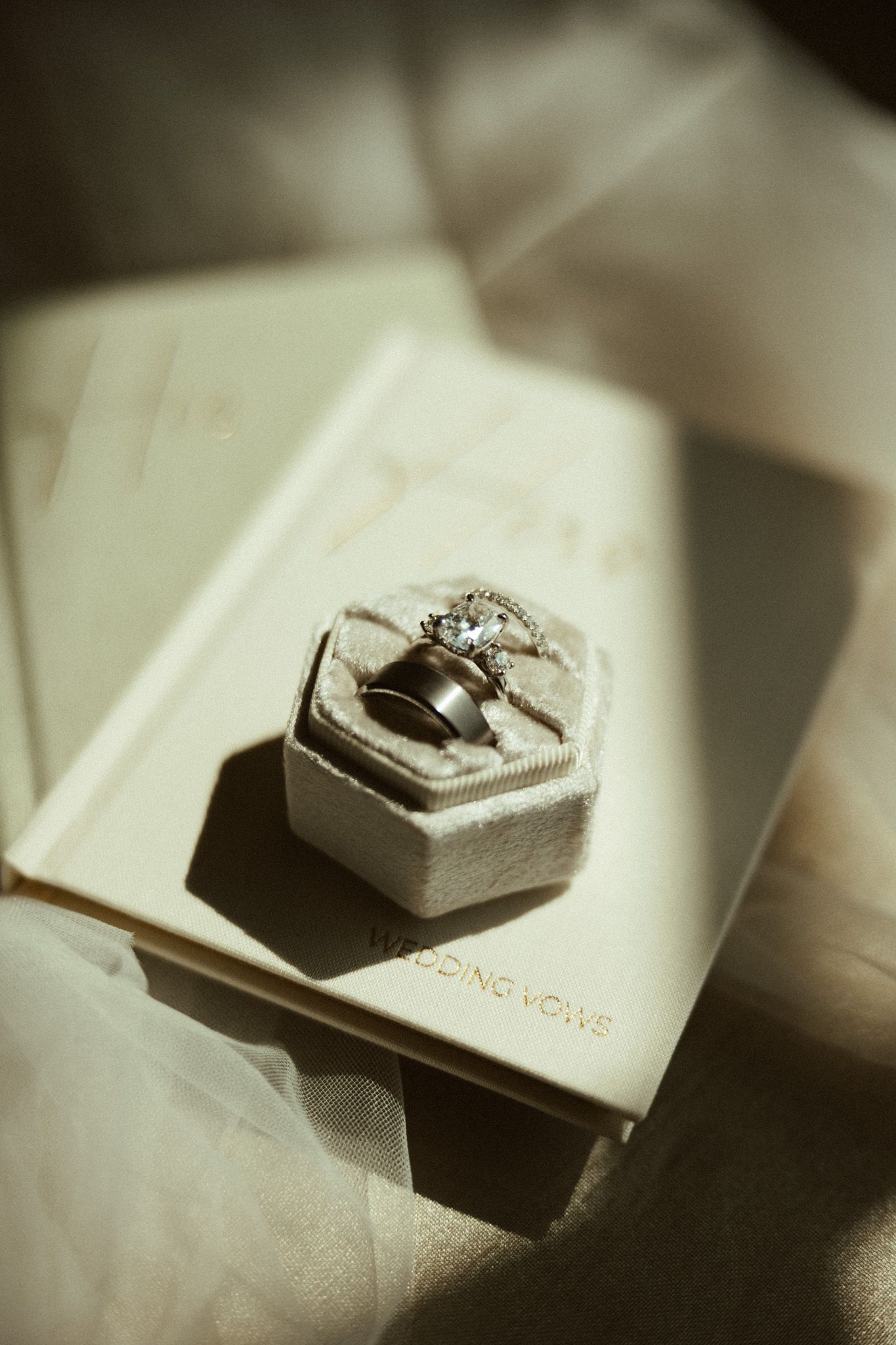 Wedding rings in a velvet hexagonal box atop a wedding vows book in soft golden light.
