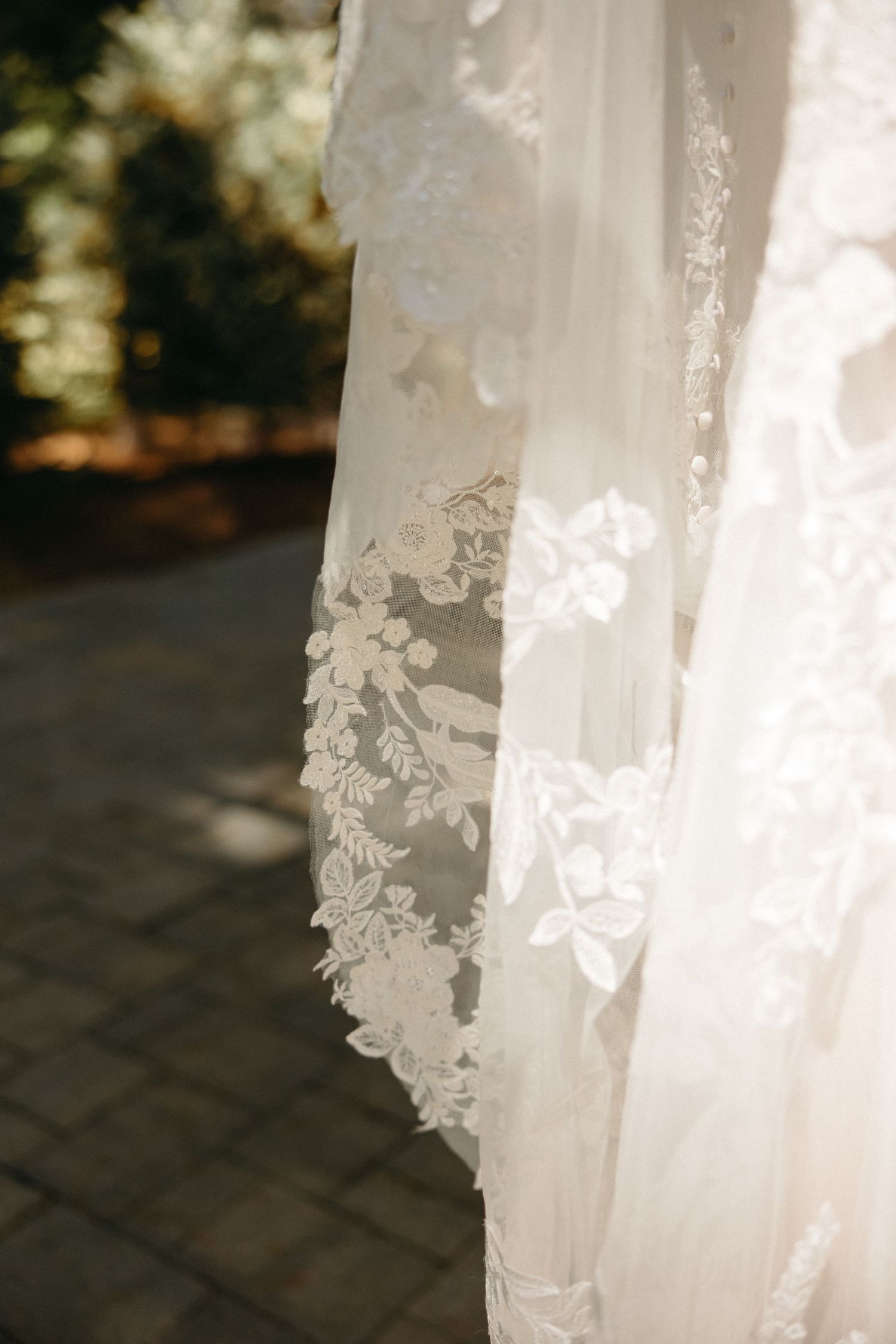Close-up detail of delicate floral lace wedding dress veil in soft natural sunlight outdoors.