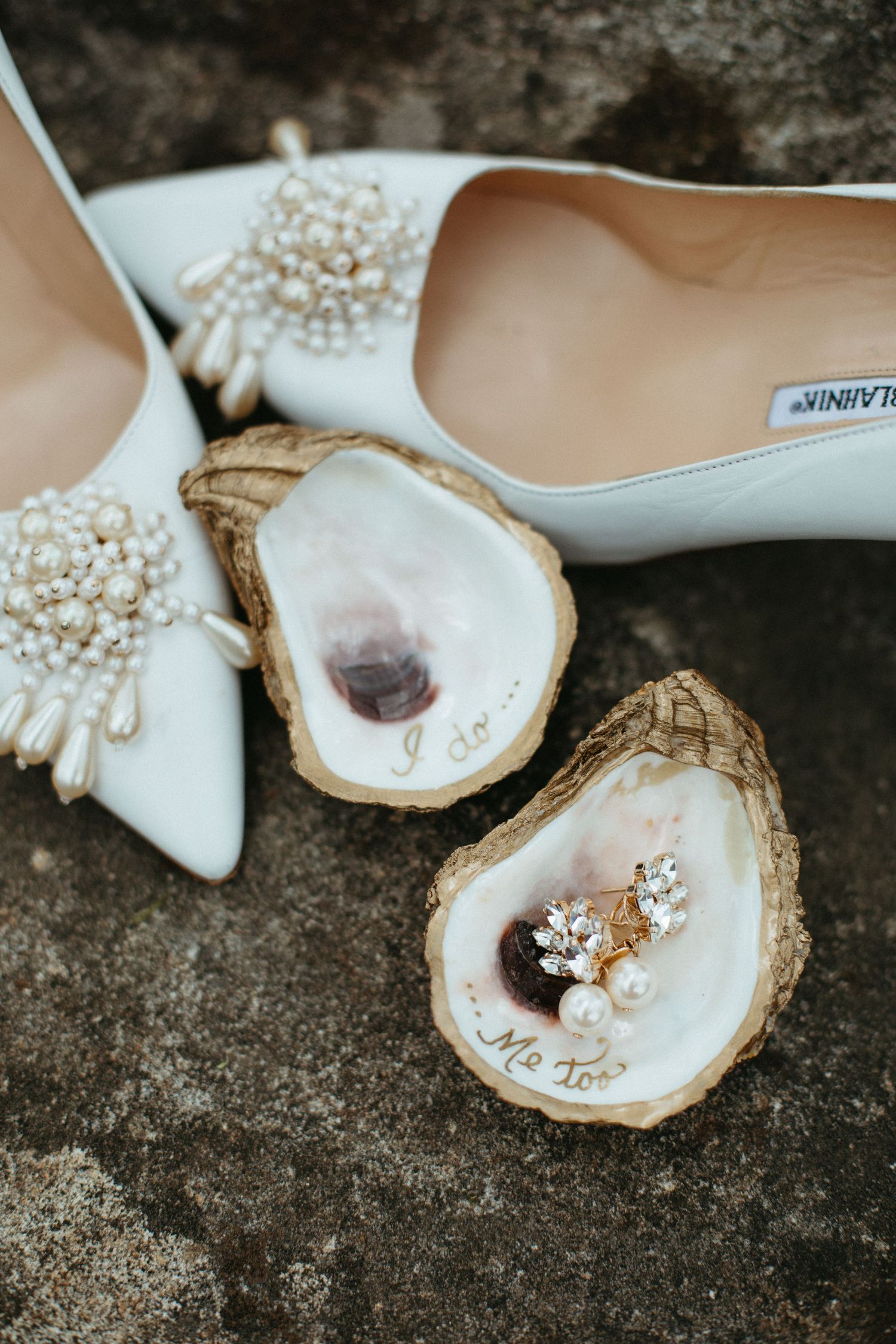 Bride in strapless white gown holds bouquet while facing groom on dramatic rocky ocean shore.
