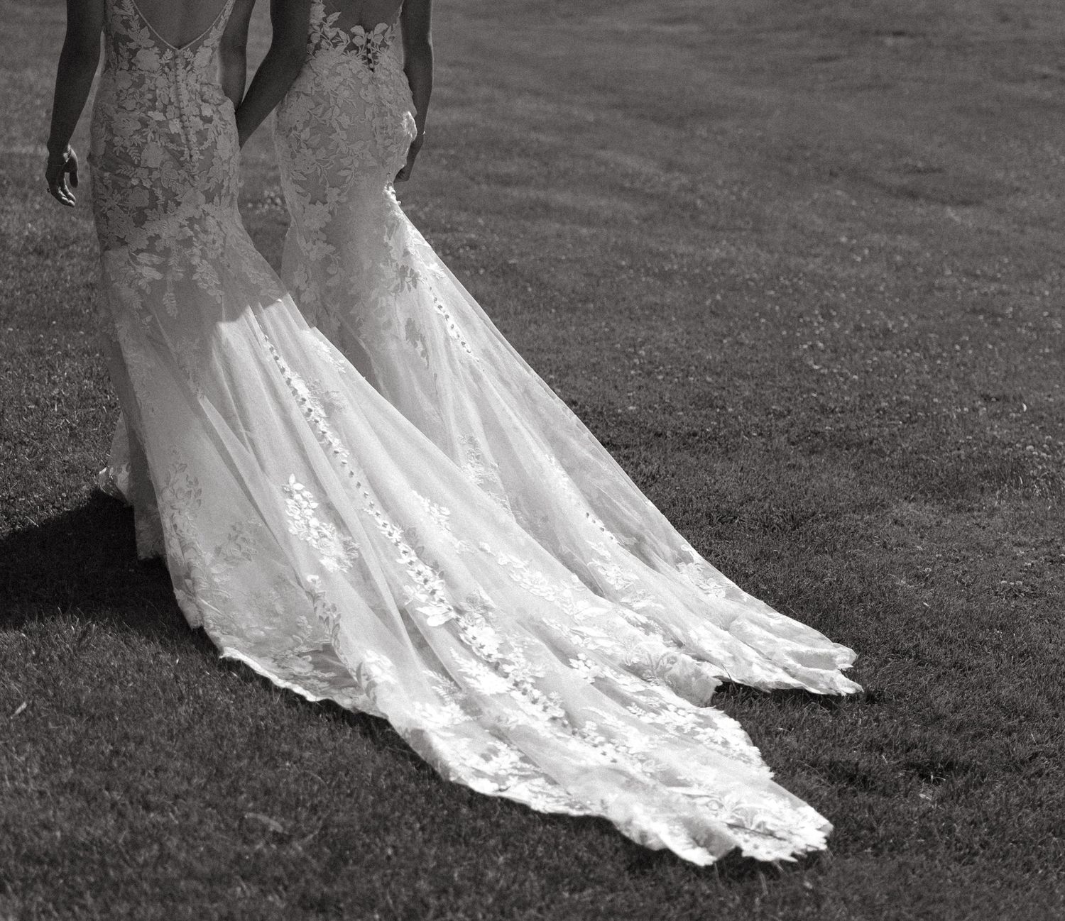 Black and white photo of a bride in a lace mermaid wedding gown with an elegant train on a lawn.