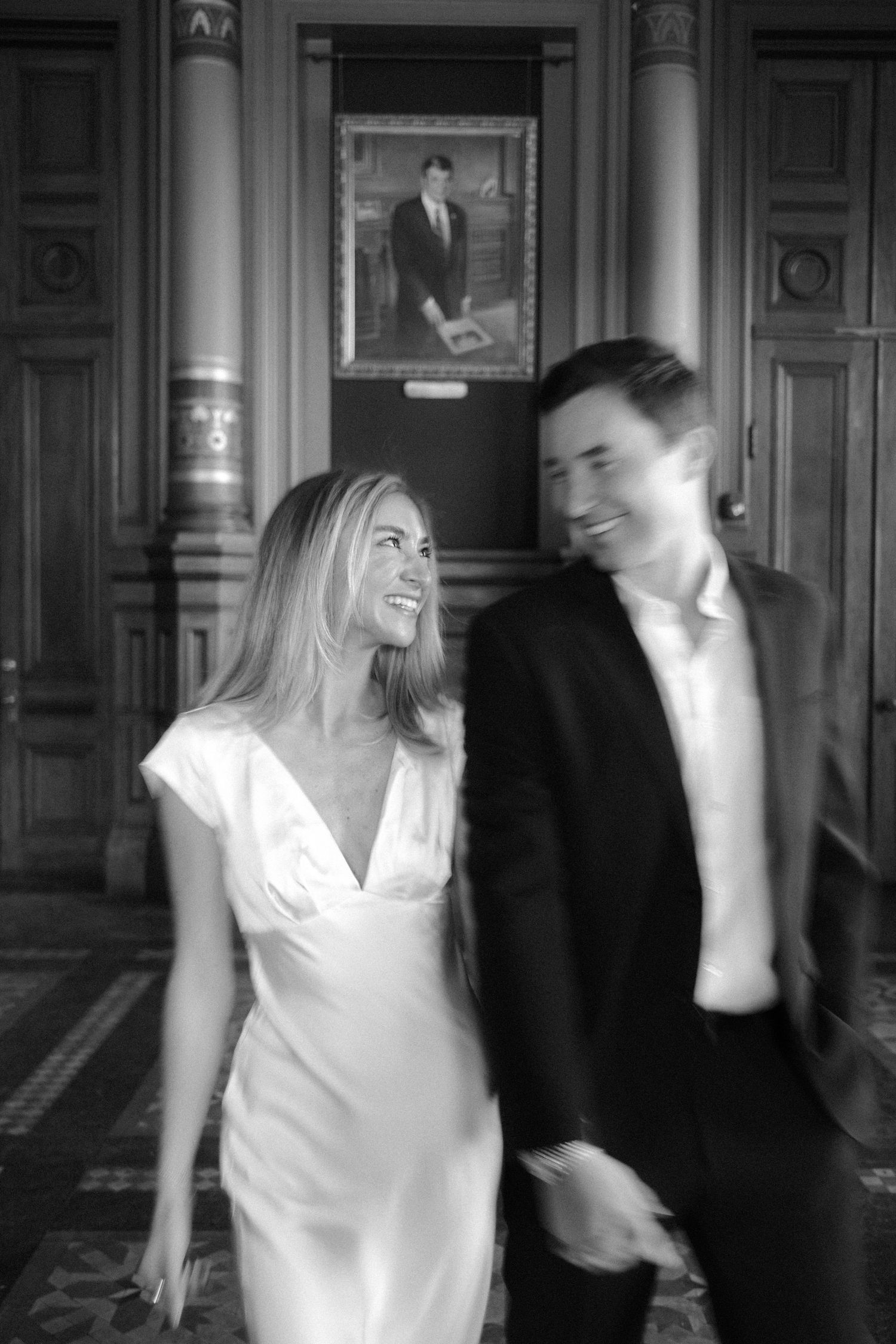 Joyful couple walking together in ornate wood-paneled room with portrait painting in background.film-inspired