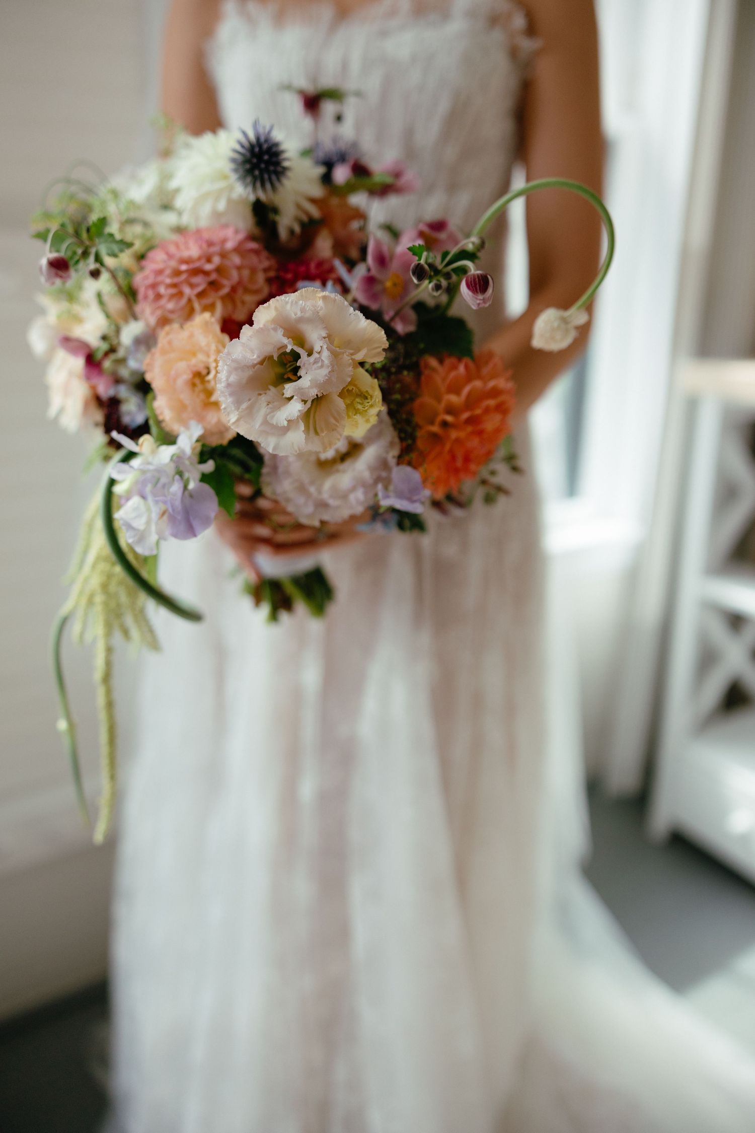 Bride in white lace gown holding a lush bridal bouquet with peach dahlias, garden roses, and wildflowers.