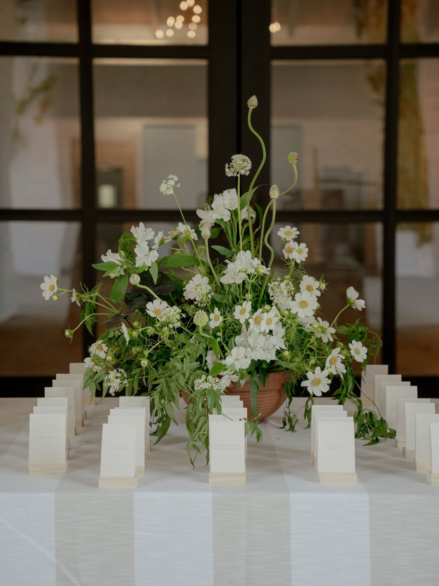 Elegant white floral arrangement with place cards displayed on white tablecloth.