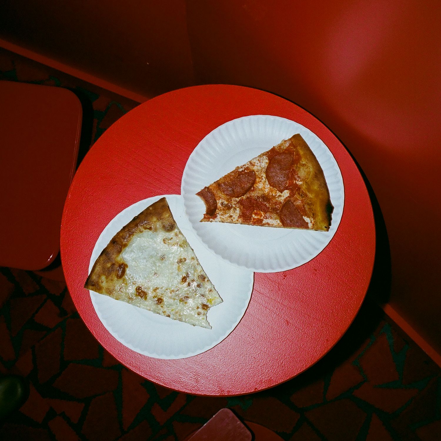 Paper plates with partially eaten pizza slices on a red table.