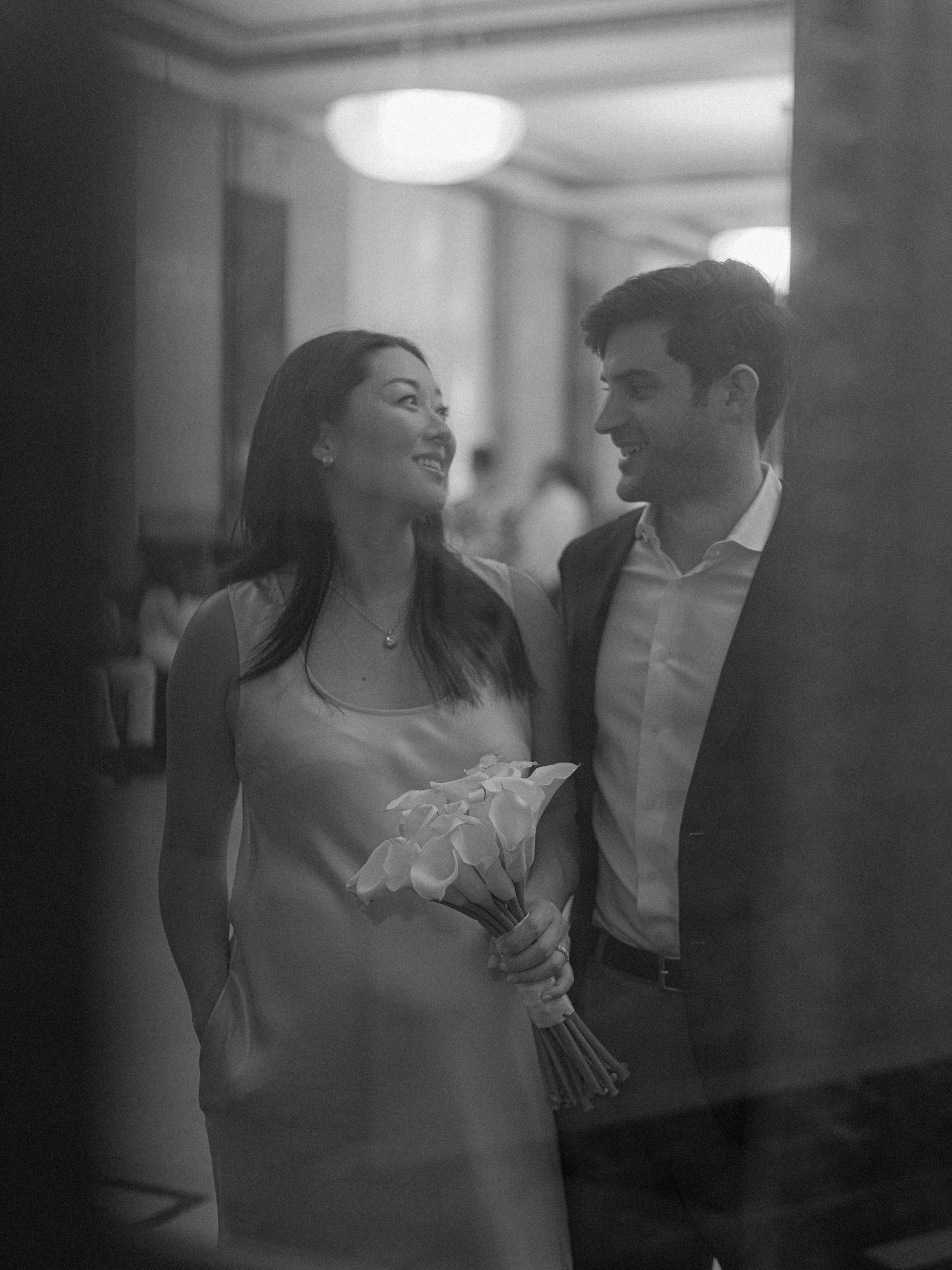 A candid black and white moment captured in an elegant hallway with a chandelier.